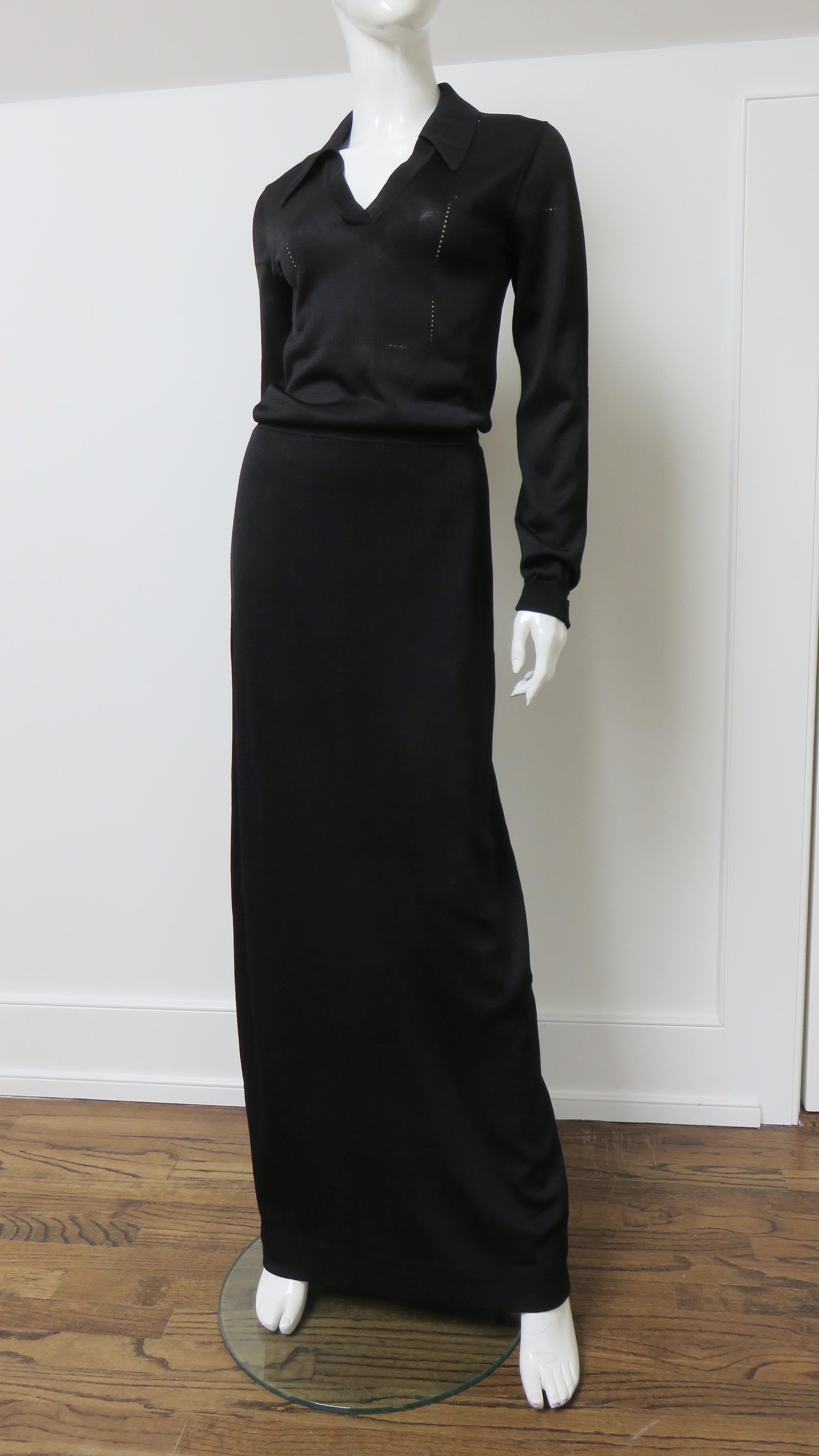 Robe noire sophistiquée en tricot longueur plancher d'Anne Fogarty, fabriquée dans le Hong Kong britannique des années 1970.  Il est doté de manches longues avec poignets repliés, d'un col chemise et d'un col en V.  Il est semi-ajusté à la taille