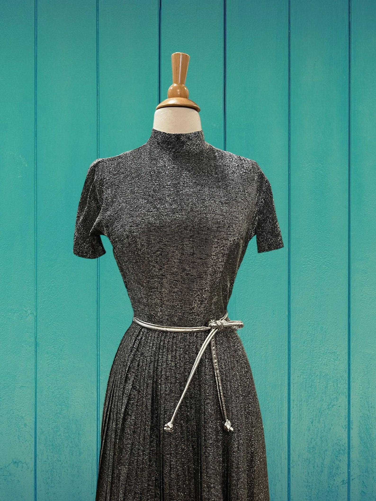 vintage Anne Fogarty metallic cocktail dress
fit & flare silhouette
dark silver lurex
mock neck collar
short sleeves
free flowing pleated skirt
falls to knee length
dress is lined
back zip closure
silver belt
excellent condition. no notable