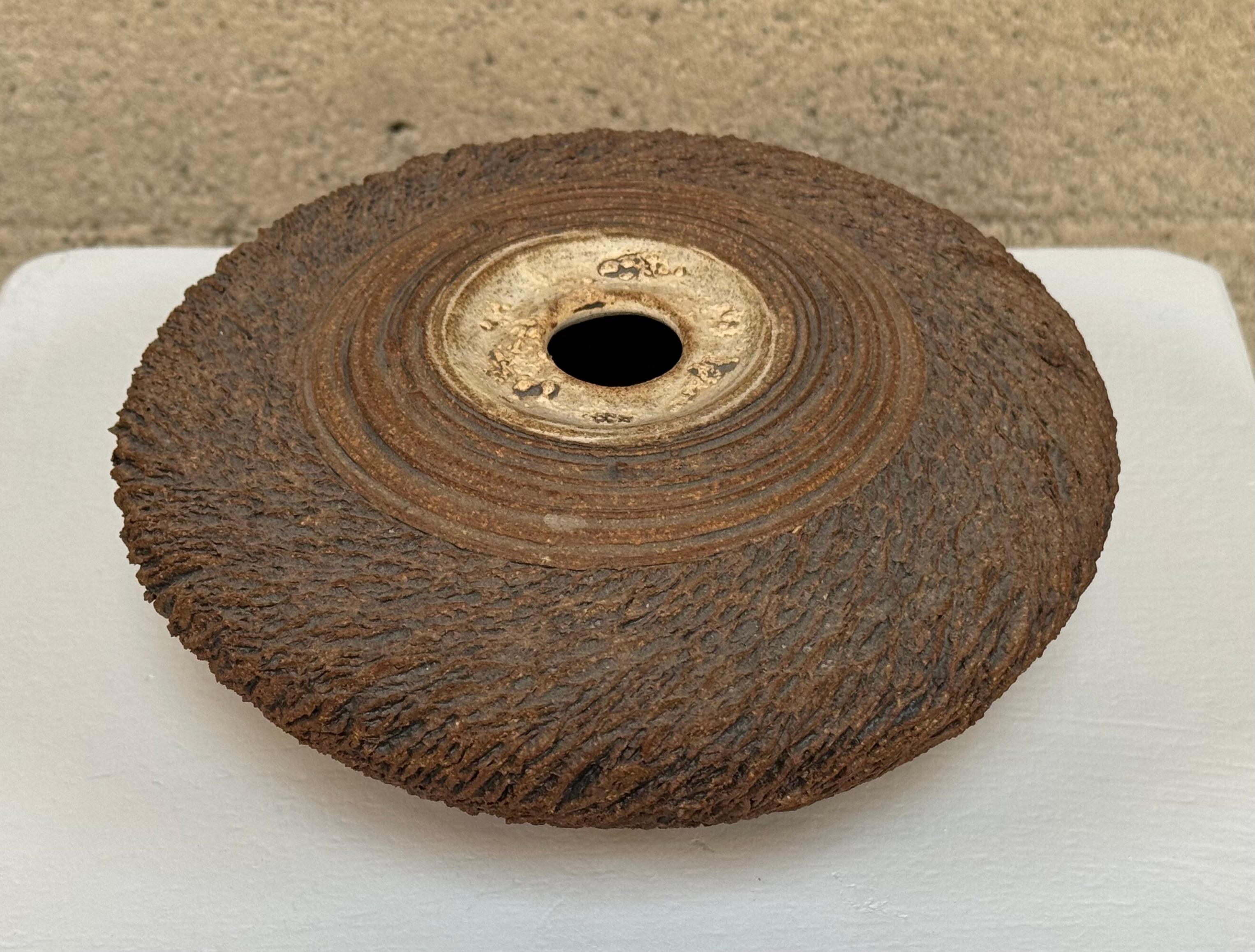 Anne Goldman è una ceramista nota per le superfici molto strutturate dei suoi pezzi, che richiedono almeno 7 fasi di lavorazione. Questo vaso affusolato ha un'apertura circolare con un bordo bianco sporco circondato da cerchi concentrici che