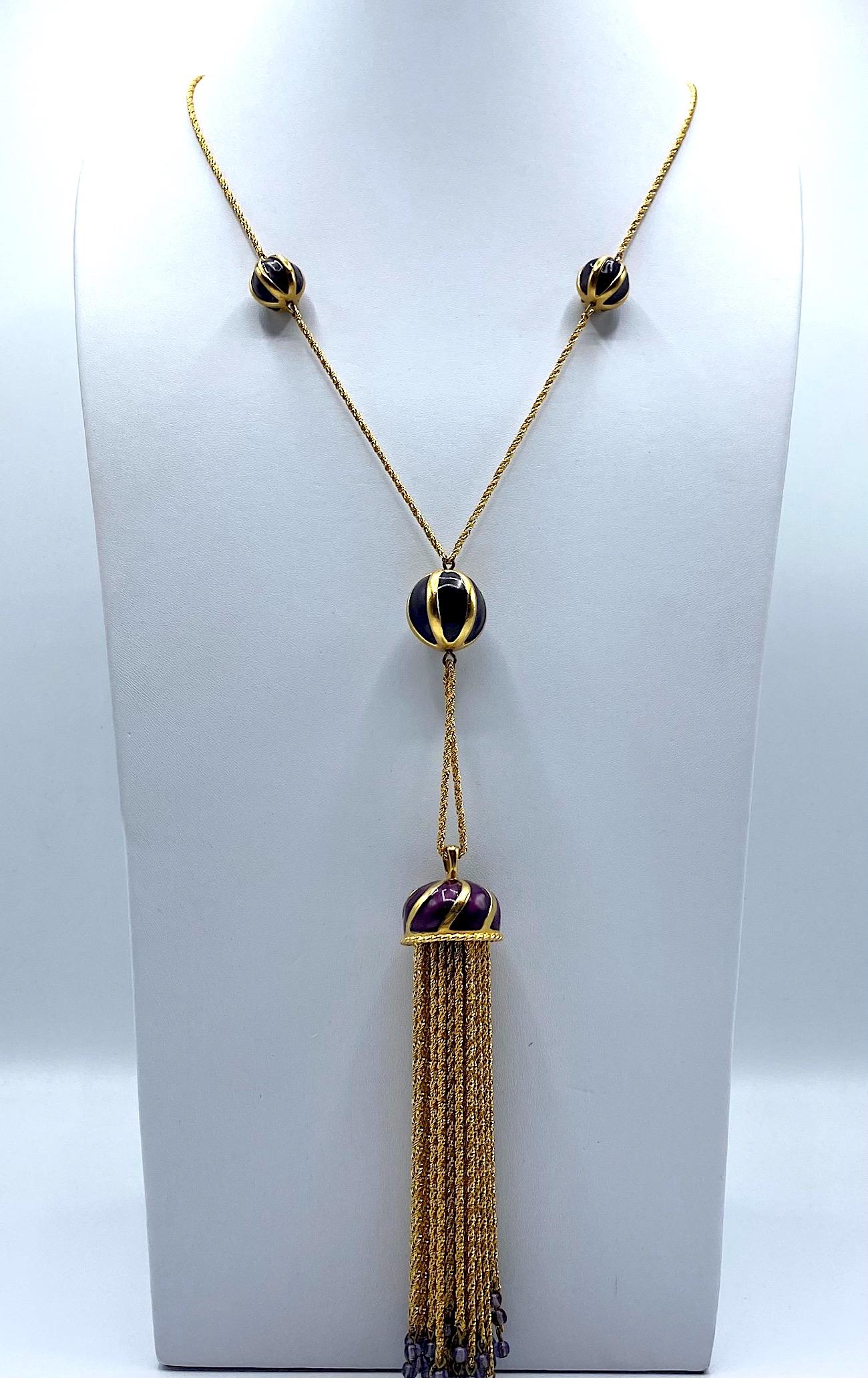 An elegant Anne Klein Couture flapper style pendant necklace circa 1990. The necklace strand and fringe are a twisted rope design in a rich gold plate. The necklace has three aubergine purple enamel and gold stripe round beads. The top two are .5 of