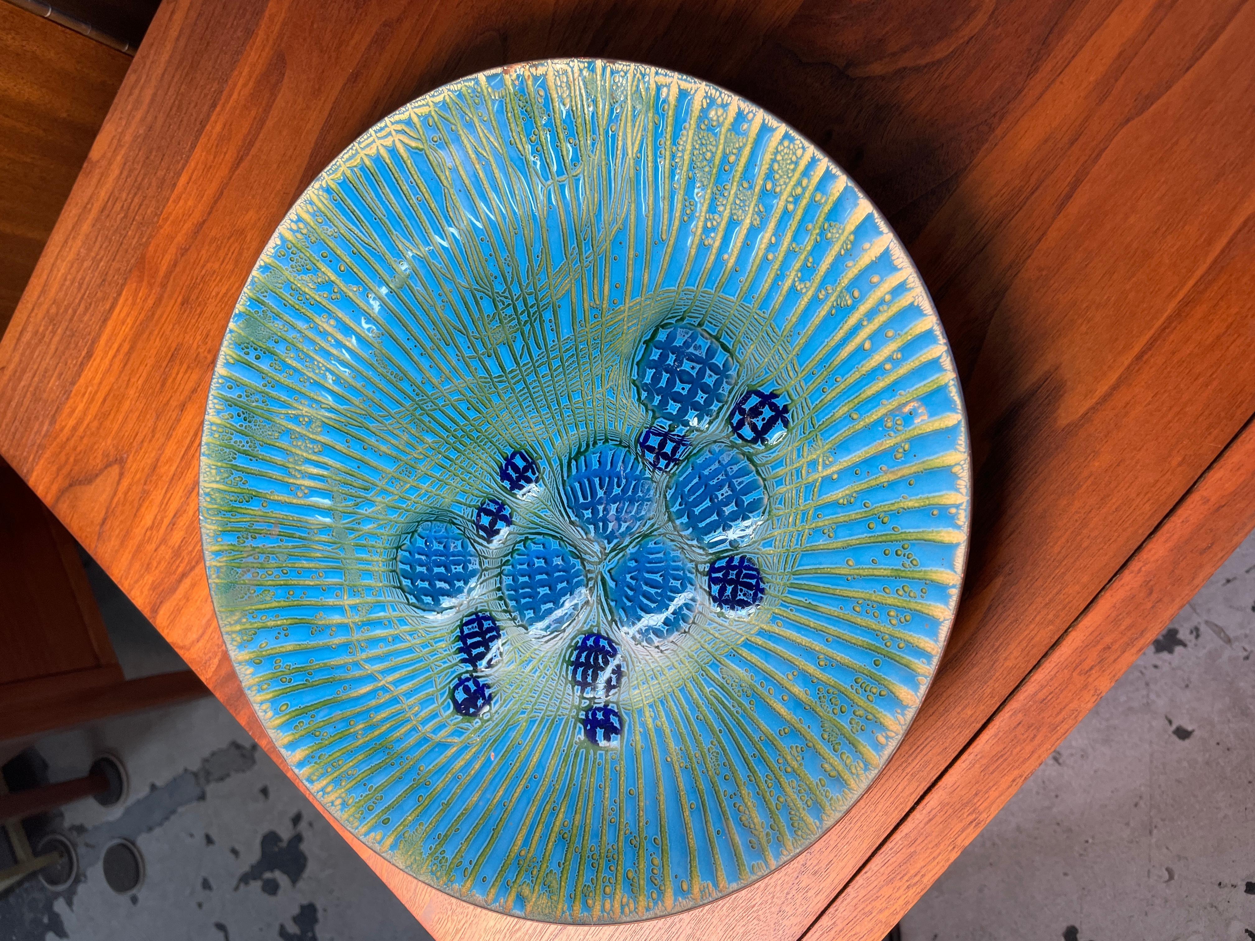 A wonderful large enameled round shaped copper plate by Annemarie Davidson of Sierra Madre. Design features incised rays emanating from the famous jewel-like structures offset from the center of plate. This pattern is sometimes known as 