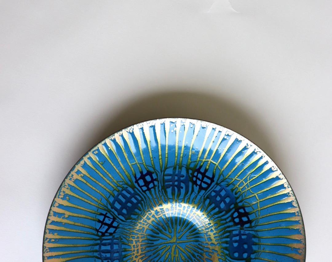 A wonderful large enameled round shaped copper plate by Annemarie Davidson of Sierra Madre. Design features incised rays emanating from the famous jewel-like structures offset from the center of plate. This pattern is sometimes known as 