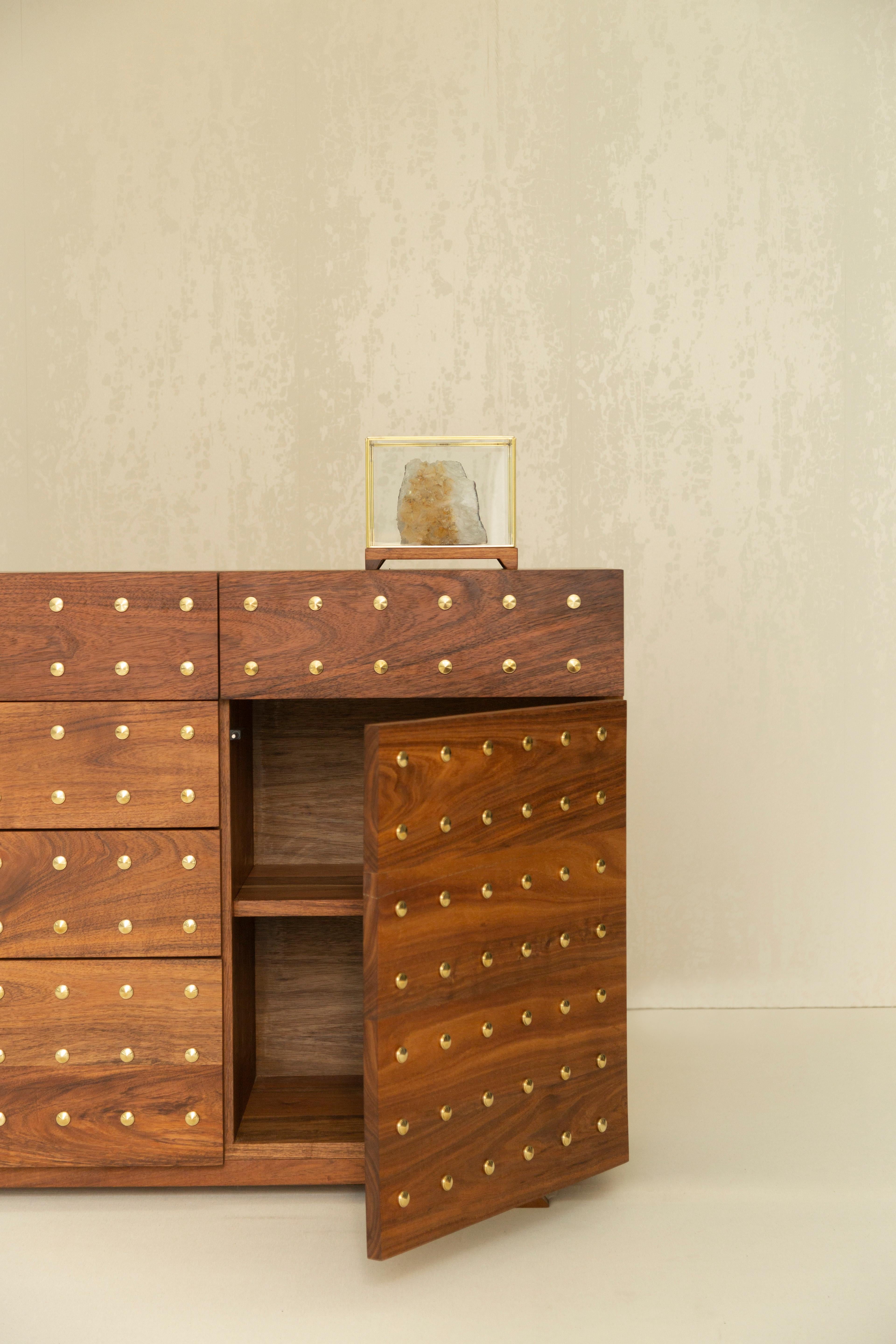 This exceptional piece, crafted from solid tzalam wood (caribbean walnut), boasts not only the inherent beauty of the wood but also features a touch of opulence with brass buttons inlaid delicately into the front of its drawers and door. 

With five