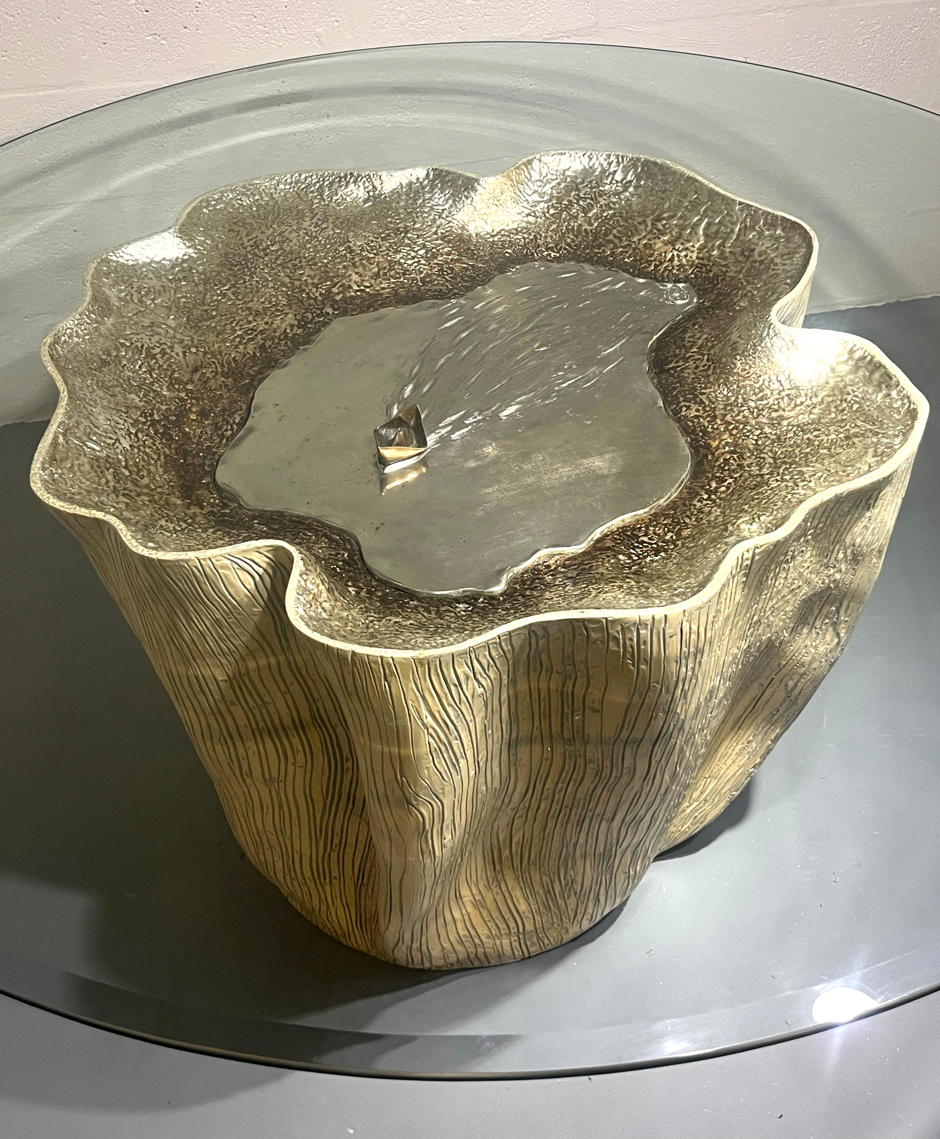A rare and poetic sculptural coffee table by Annibale Oste, Italy, circa 1980s.
The base is crafted in cast metal with a textured surface reminiscent of organic forms, resembling a tree trunk or coral structure. At the center, a polished basin-like