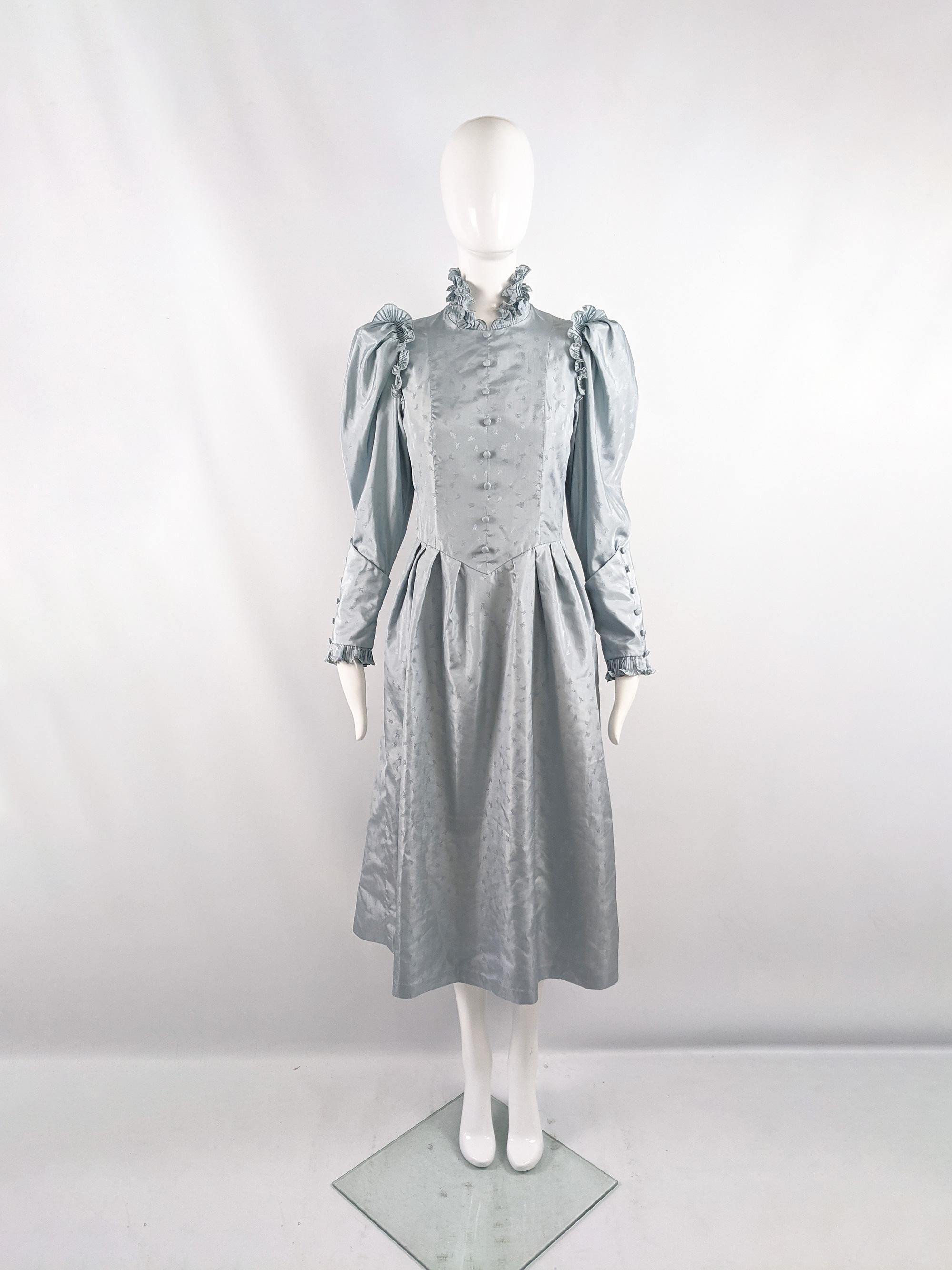 A stunning and rare vintage womens mid length dress from the 70s by iconic British boutique designer, Annie Gough. In a duck egg blue taffeta with a jacquard weave throughout. It has a pleated, ruffle high neck collar, leg o mutton style sleeves