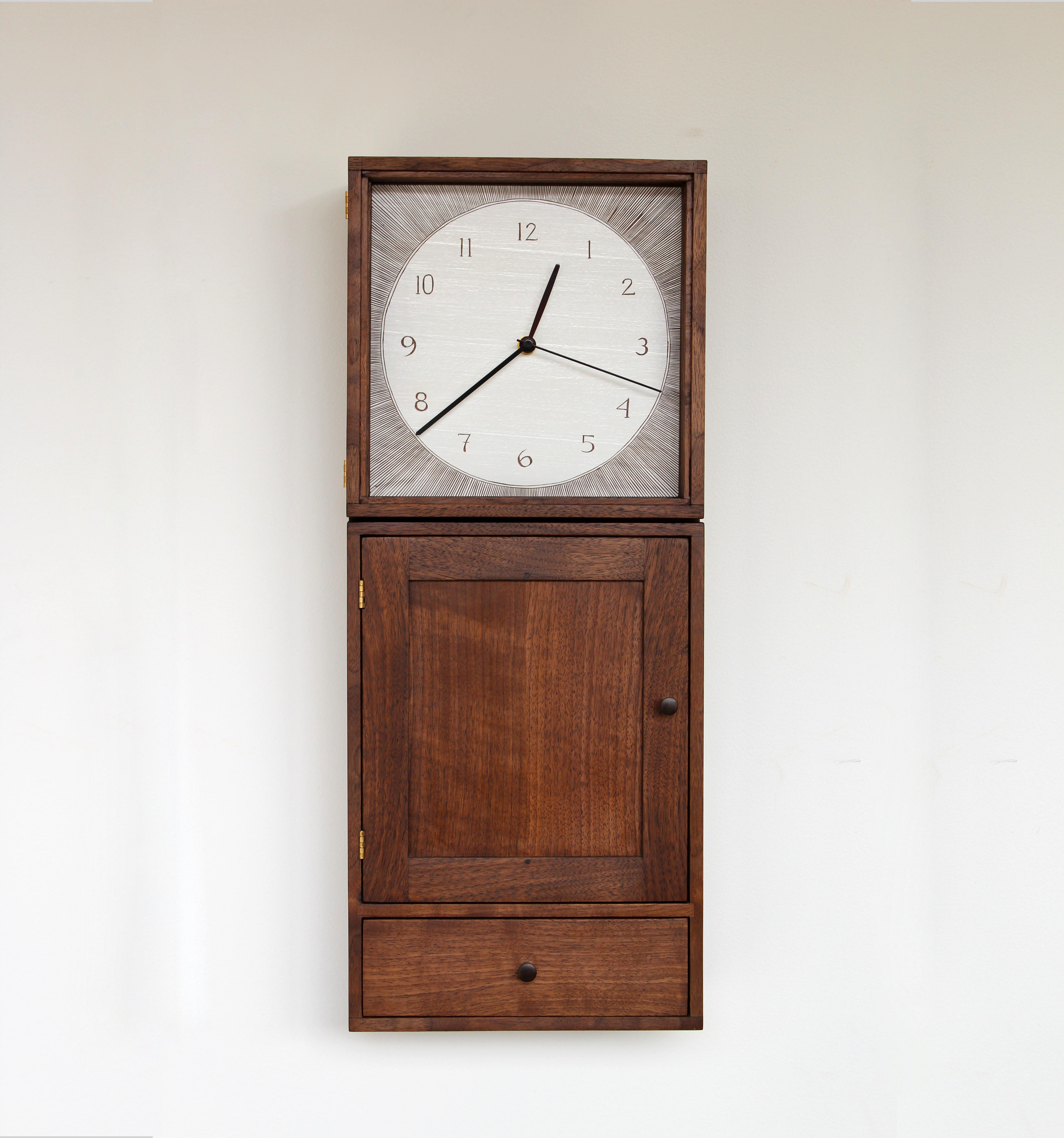 The Anniversary Clock is a contemporary take on a traditional Shaker wall-mounted clock cabinet. This updated form features hand-cut dovetail joinery, a painted and carved wooden clock face, and polished walnut pulls and pegs. The cabinet includes