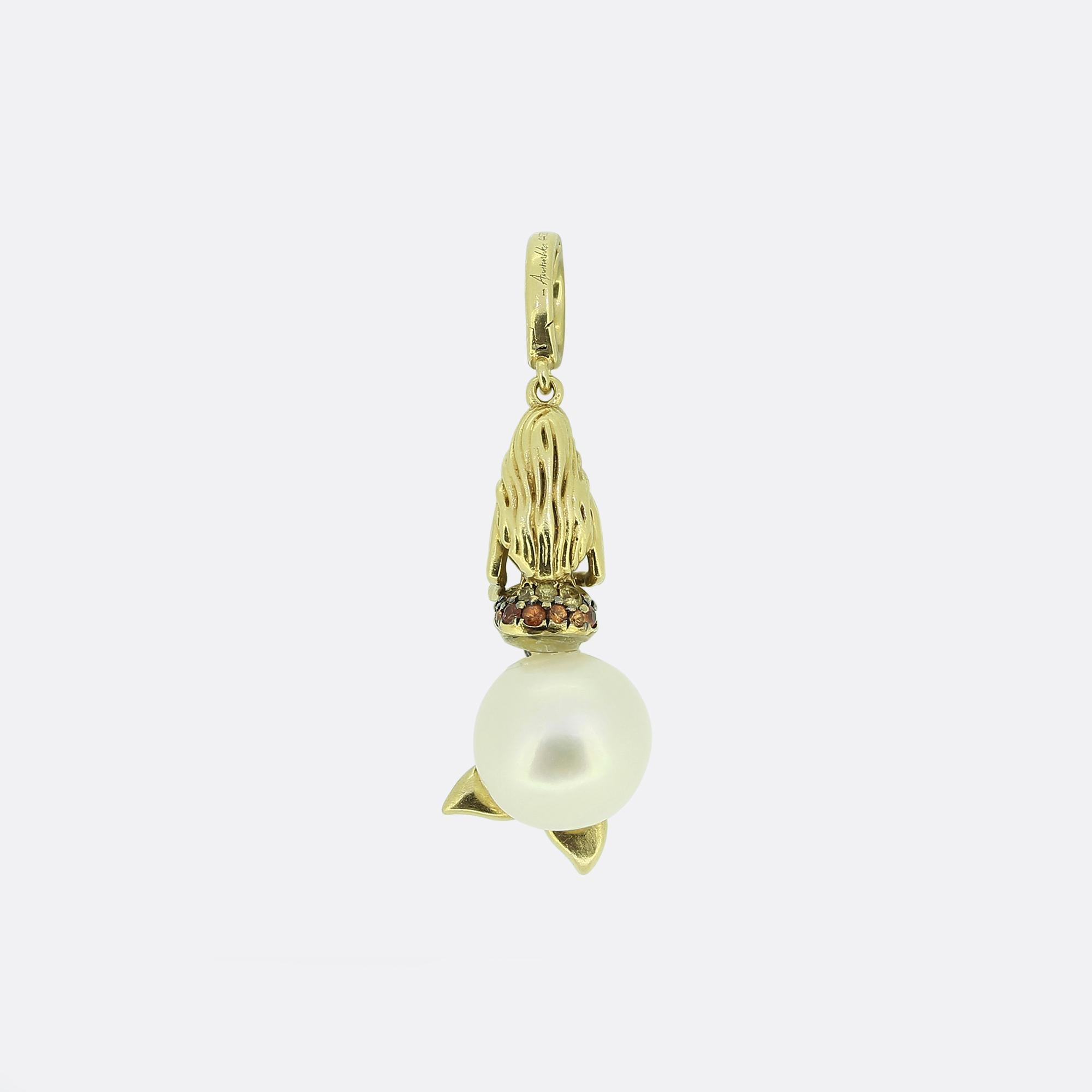 Ecco un delizioso charme in oro giallo 18ct di uno dei più apprezzati designer britannici di gioielli moderni, Annoushka. Il ciondolo mostra il disegno di una sirena appollaiata su una perla bianca rotonda e lucente. La coda della sirena è ornata da