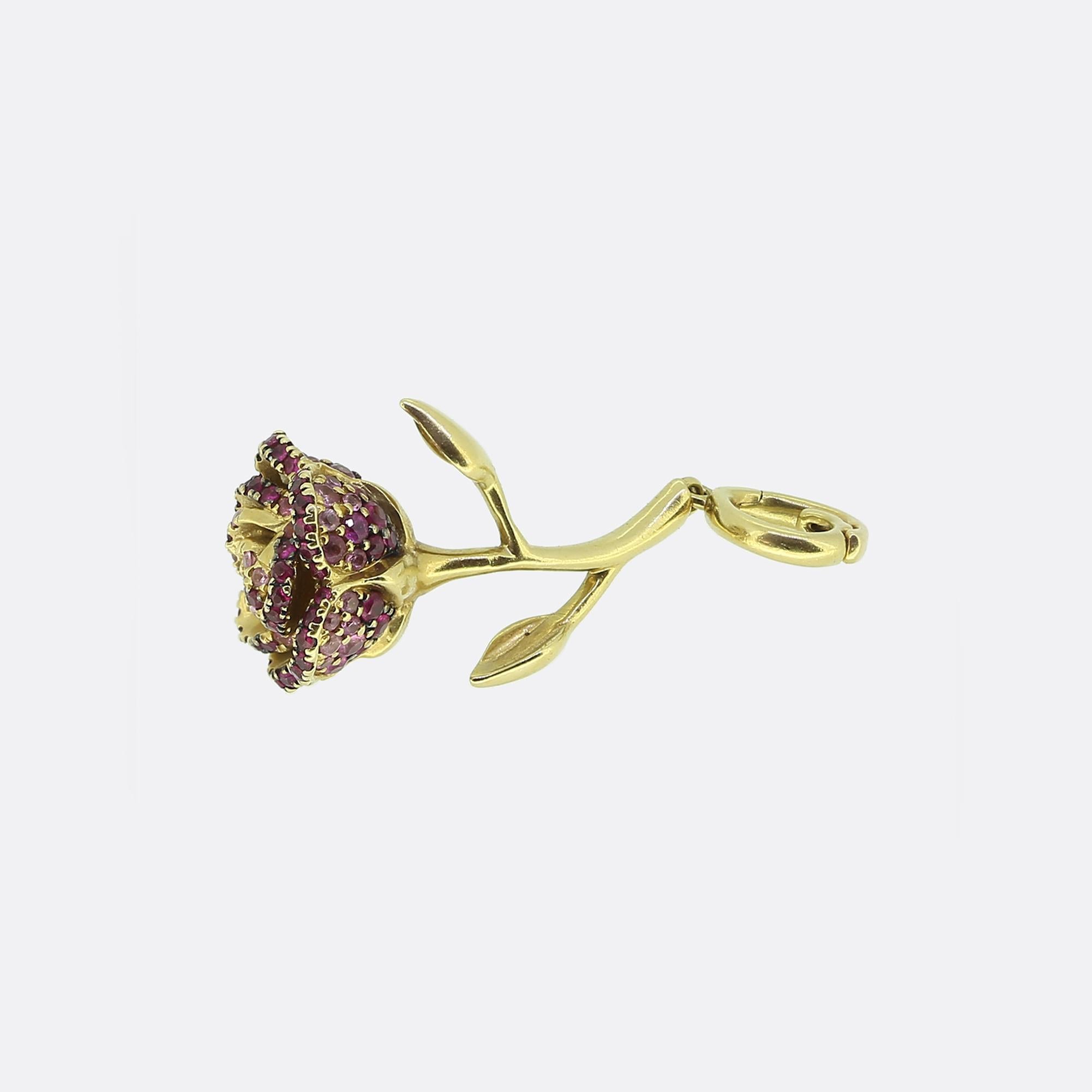 Here we have a captivating 18ct yellow gold charm from one of Britain's most esteemed modern jewellery designers, Annoushka. This piece features a delicate rose design with a gracefully curved stem and leaves. The rose is adorned with vibrant red