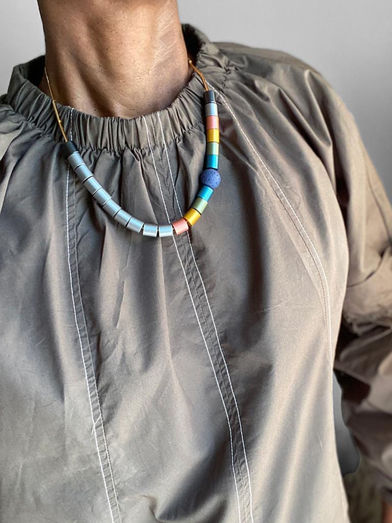 Anodized  Aluminum Necklace with Bold Satin Finish by Trecy Bleich

Anodized aluminum with a bold satin finish.  The necklace is color-blocked to mimic a vintage look.  The round polyester resin bead is made to look like coral but with the peace of
