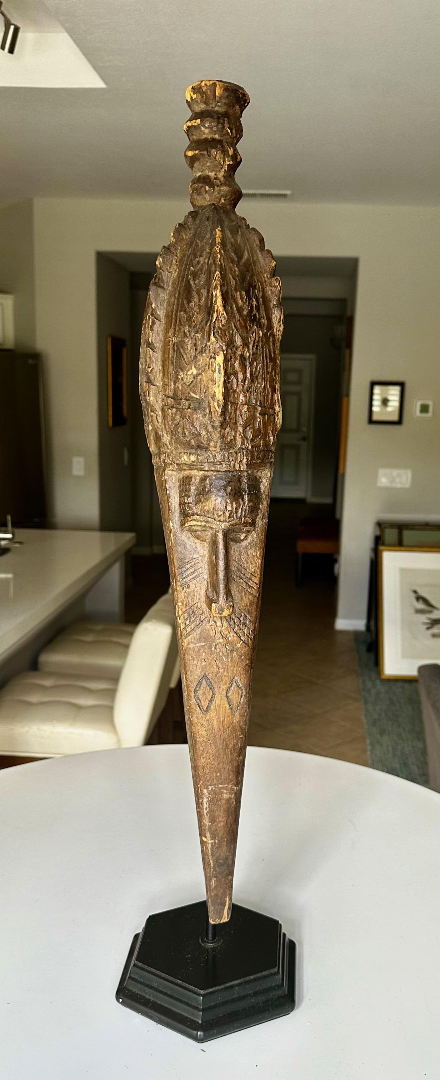 An antique Baga anok or elek carved wood mask sculpture, with bird and human face form elements, made by Baga people (Guinea West Africa). Features long and pointed bird beak, incised carvings, and carved human face. The sculpture sits on a newer
