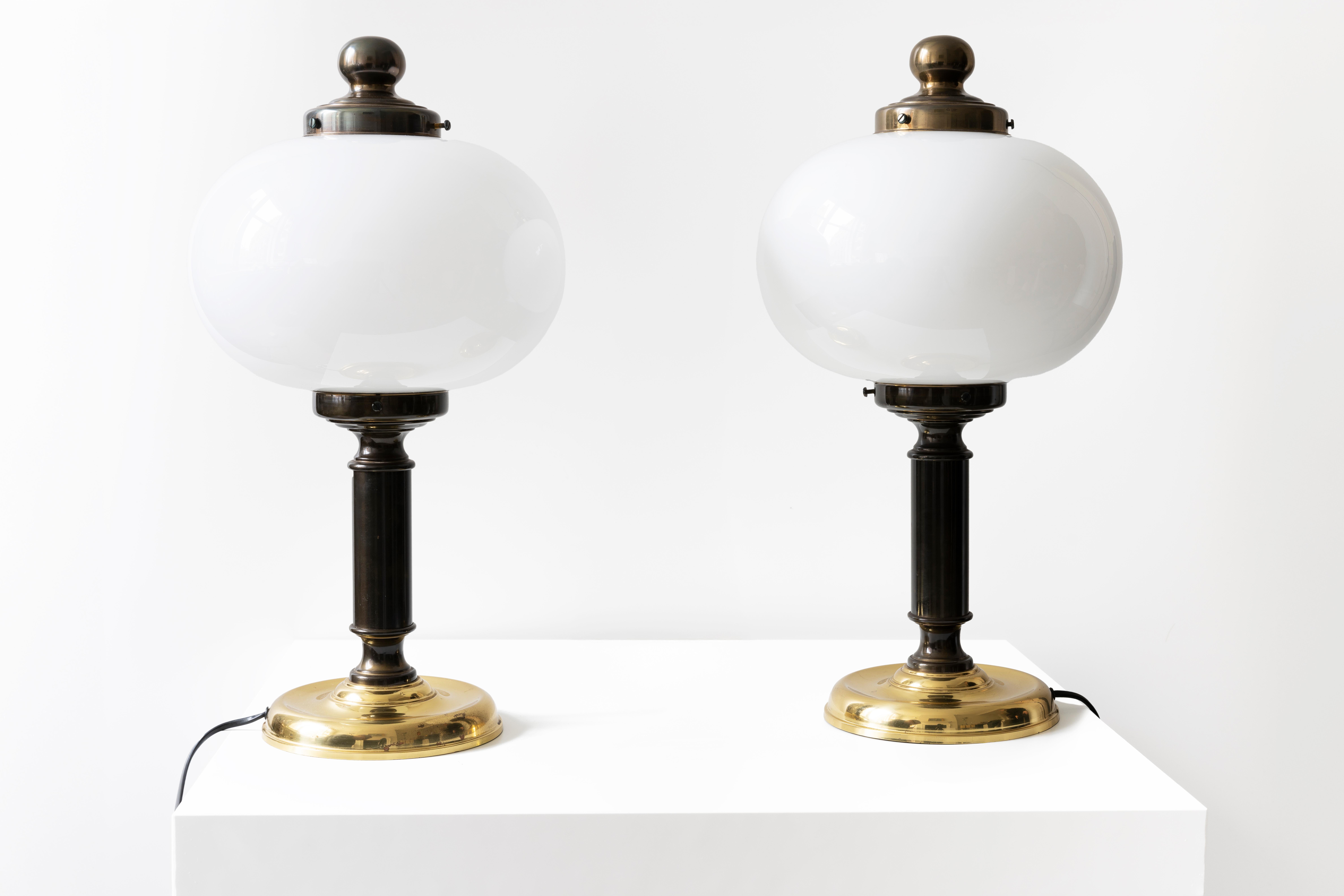 This beautiful and unique pair of 1980 table lamps has a classic design in metal with a rounded white opaline shade that exudes a soft, warm glow. The bases are adorned with a rich brass finish, adding a touch of elegance and sophistication. The