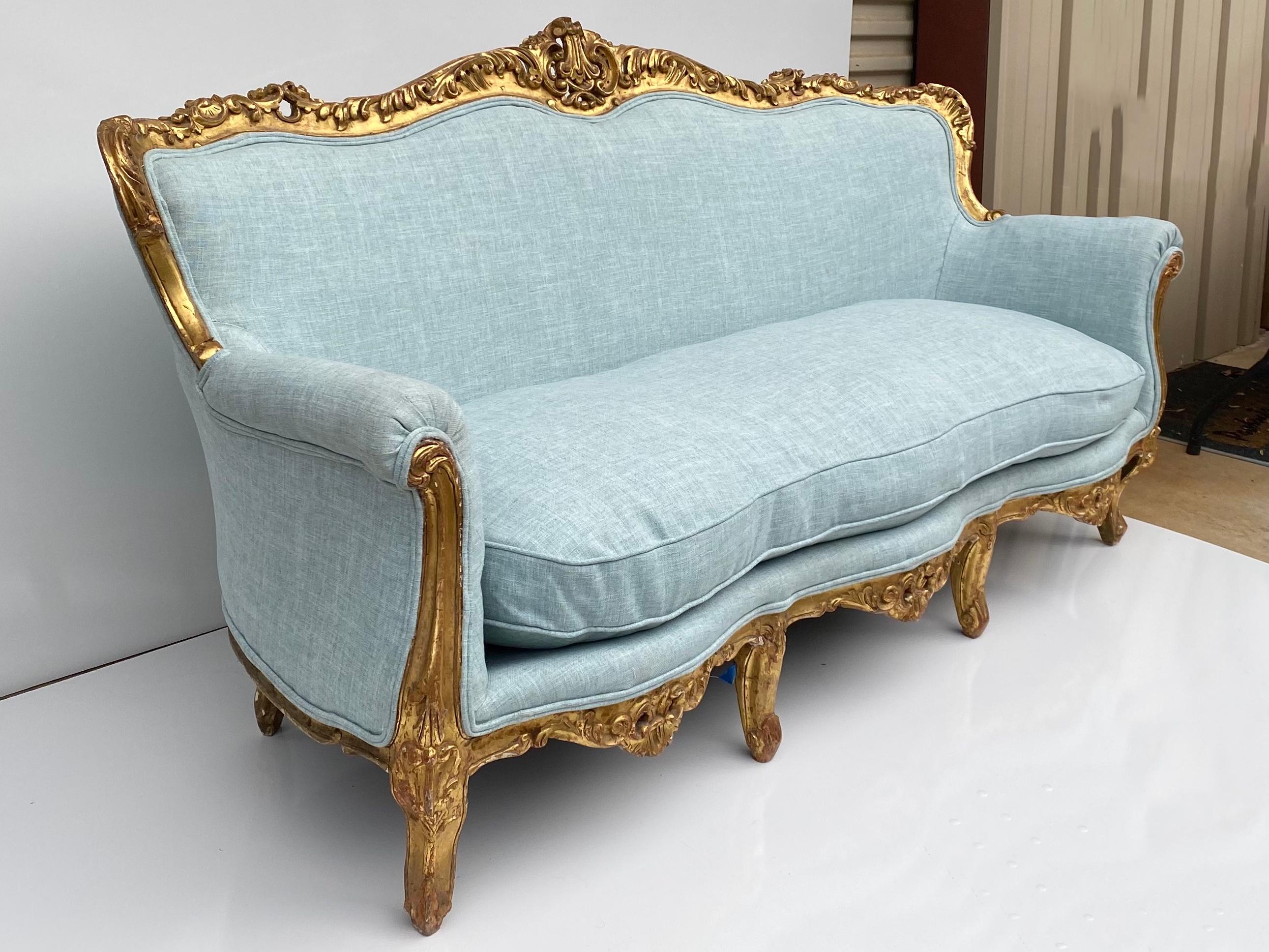 Love this! This is an antique French sofa or canapé with a carved water gilt frame. The frame does show some age appropriate wear. The upholstery is a new turquoise/blue linen. The cushions are down. Measures: Seat 19” H, arm 26.5” H. SD 22”.