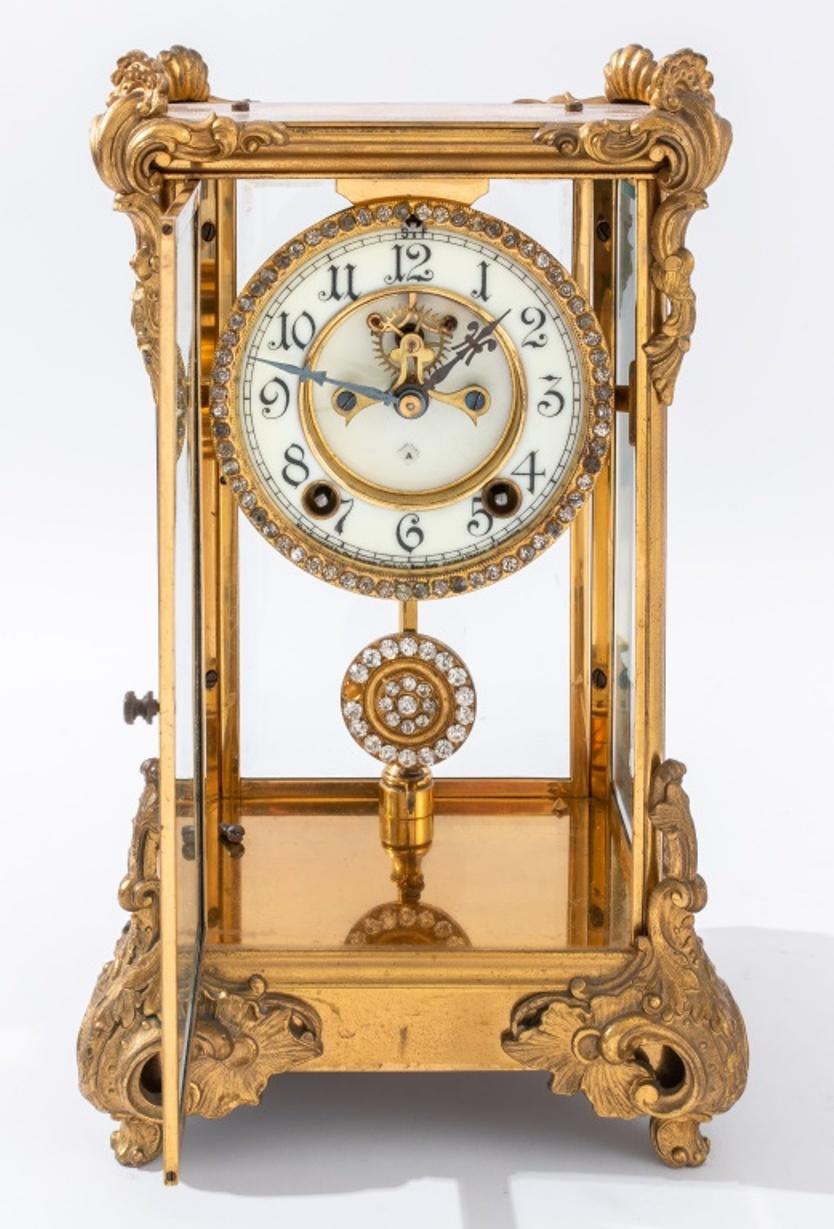 Ansonia Marquis Crystal regulator, ca. 1904, with an eight day time and strike with open escapement, jeweled pallets, and a paste-set bezel and pendulum, within a gilt bronze rococo revival case (finial lacking), the face signed 