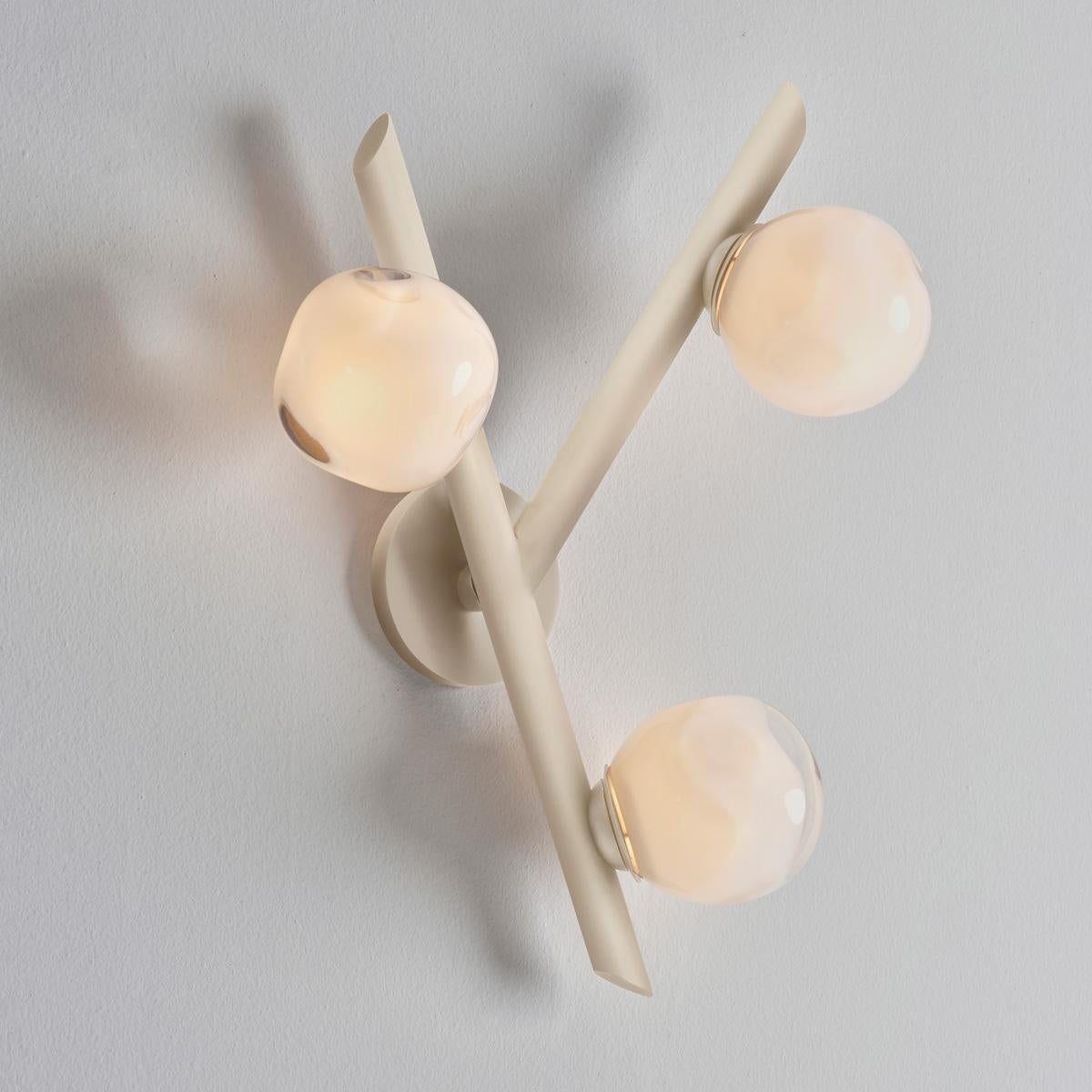The Antares wall light harmoniously balances the linear details of its intersecting arms with the organic form of its handblown glass shades. The first images show the fixture in our Sand White finish-subsequent pictures show it in a selection of