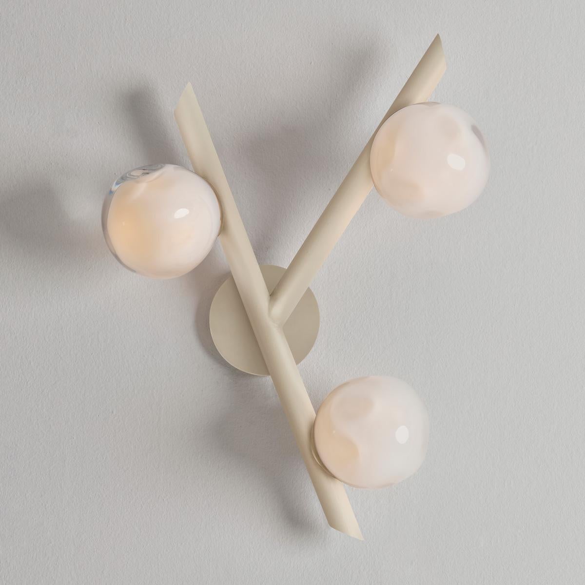 The Antares wall light harmoniously balances the linear details of its intersecting arms with the organic form of its handblown glass shades. The first images show the fixture in our Sand White finish-subsequent pictures show it in a selection of