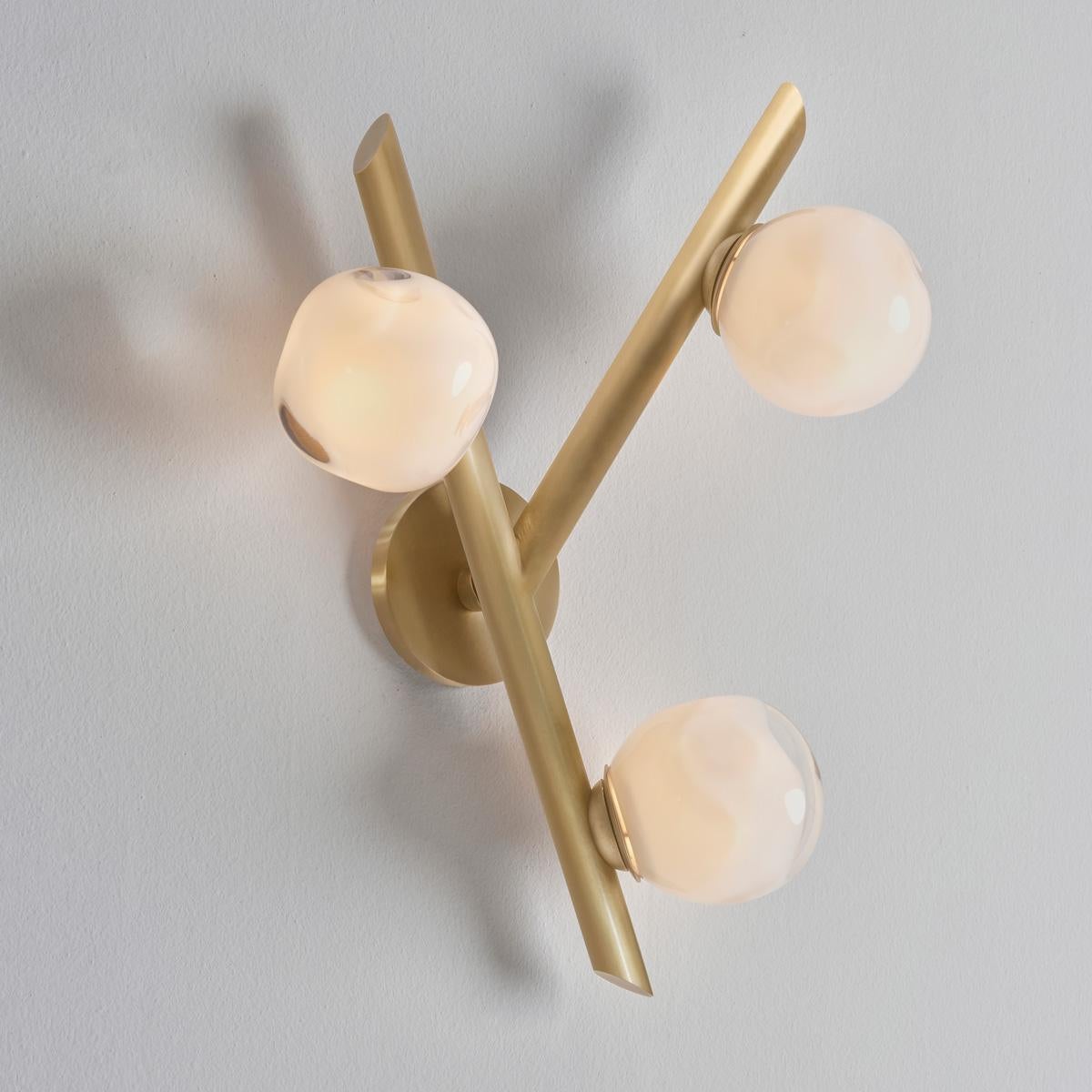 The Antares wall light harmoniously balances the linear details of its intersecting arms with the organic form of its handblown glass shades. The first images show the fixture in our satin brass finish-subsequent pictures show it in a selection of