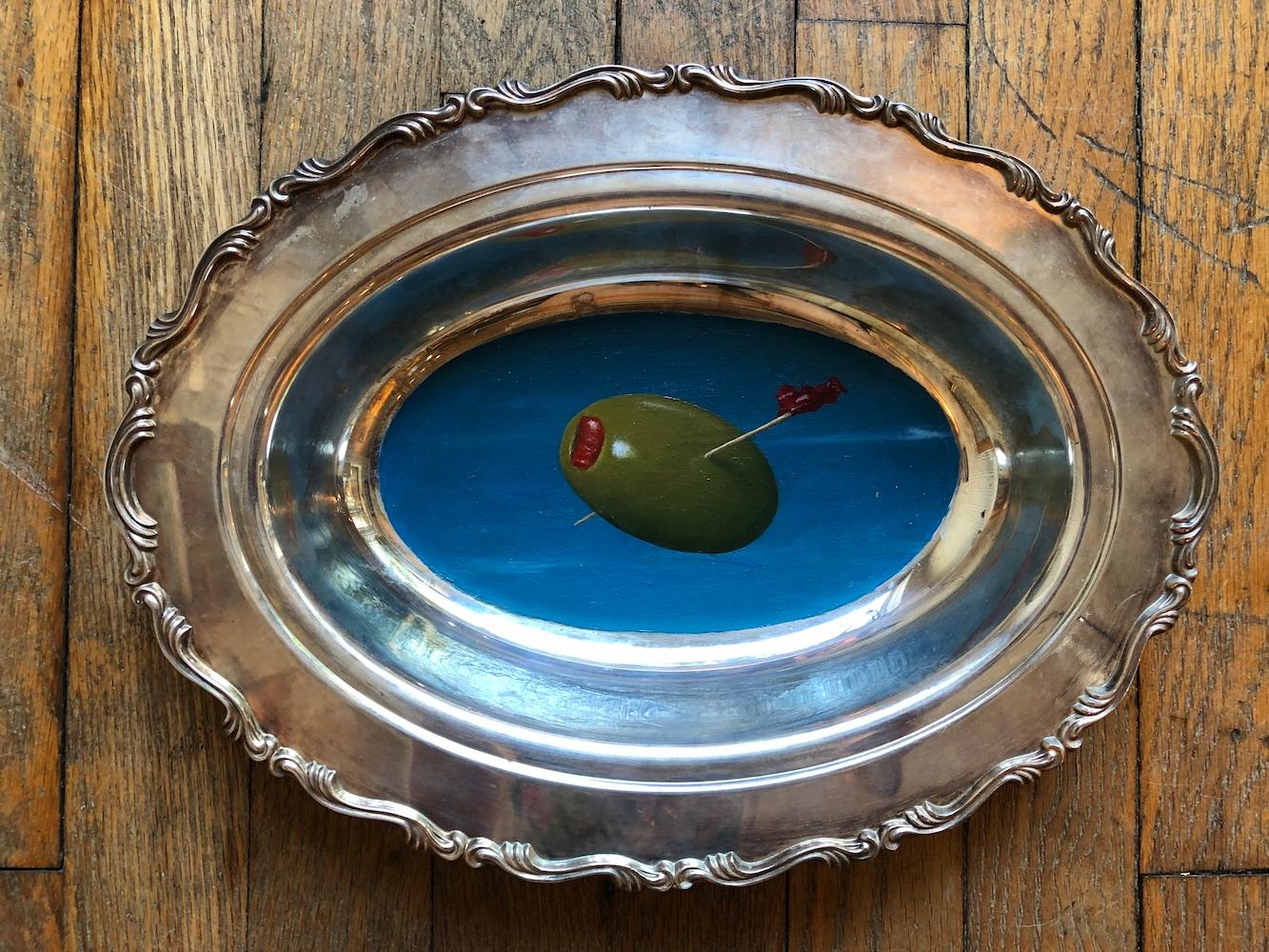 Anthony Ackrill Still-Life Painting - "Olive" surrealist oil painting on silver tray of cocktail olive floating in sky