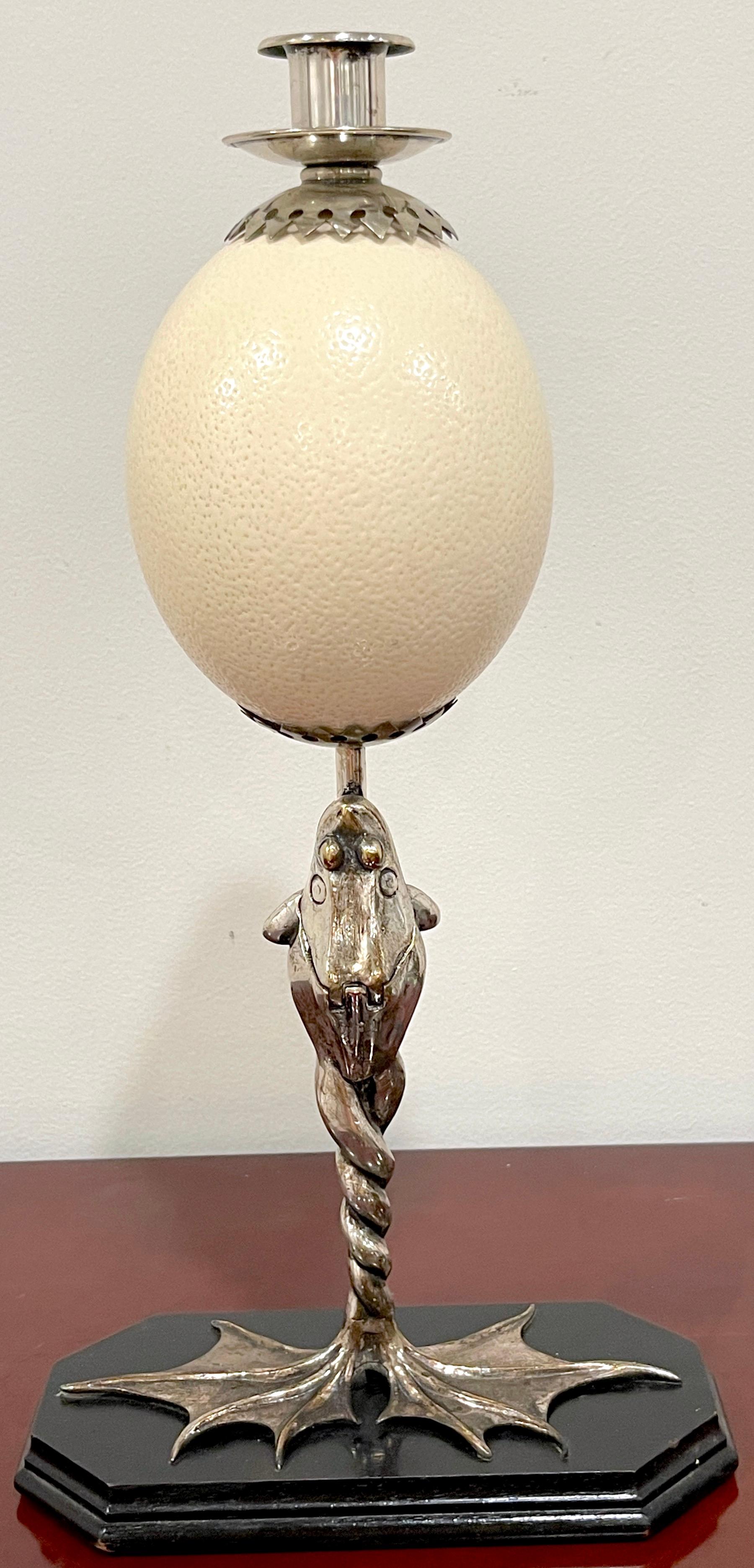 Anthony Redmile Silverplated Figural Frog Mounted Ostrich Egg Candlestick
Stamped 'Redmile London'
London, Circa 1970s 
Fashioned as a standing a 17.5 -inch high silverplated -brass frog with intertwined legs, fitted with a hinged match compartment,