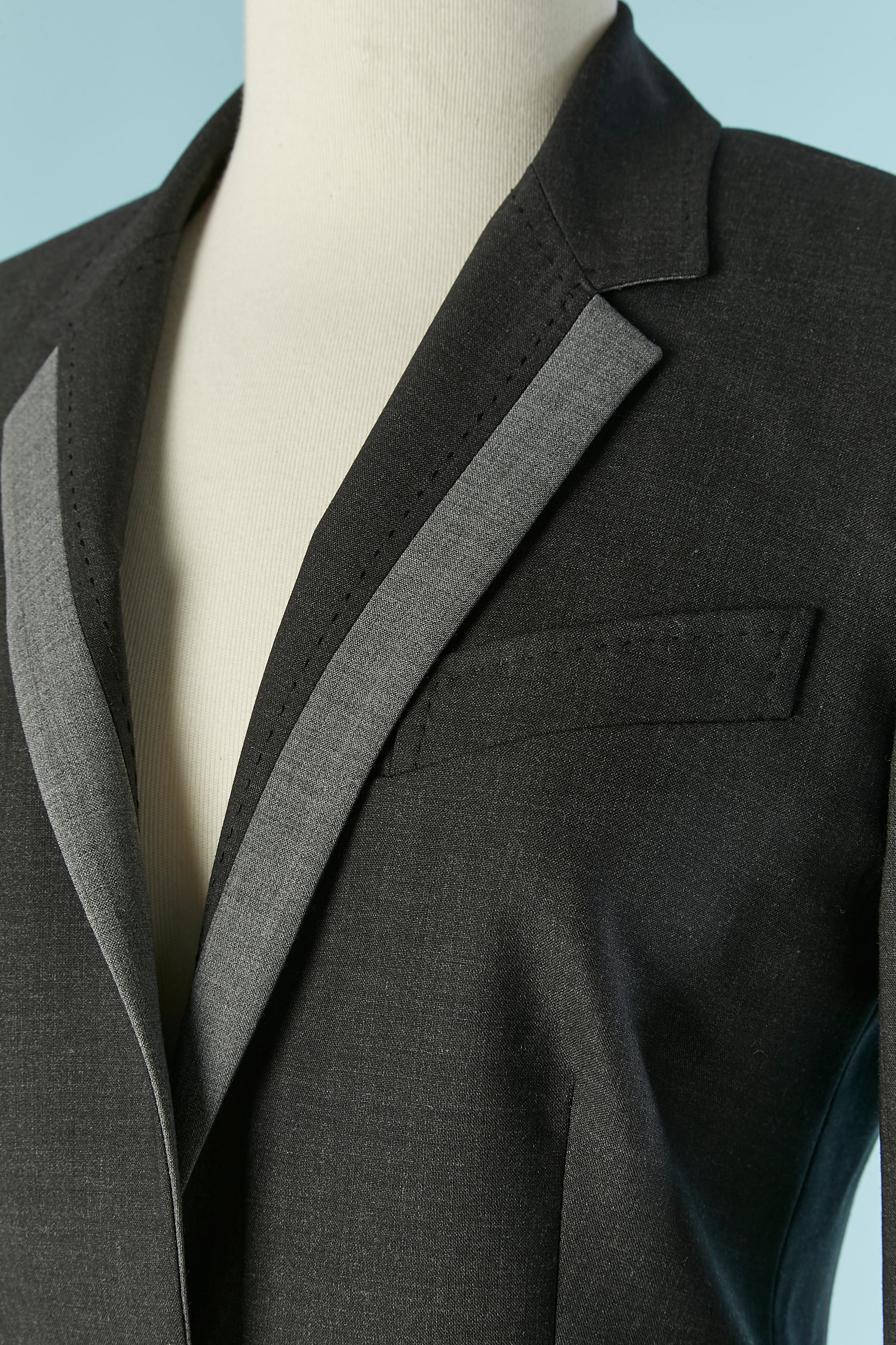 Grauer einreihiger Blazer mit hellgrauem Rand. Zusammensetzung des Hauptmaterials: 98% Wolle, 2% Elastan. 
Bedrucktes Multicolor-Futter: 100% Viskose
2. Futter ( schwarz auf der Innenseite der Vorderseite und der Ärmel ) : 100%