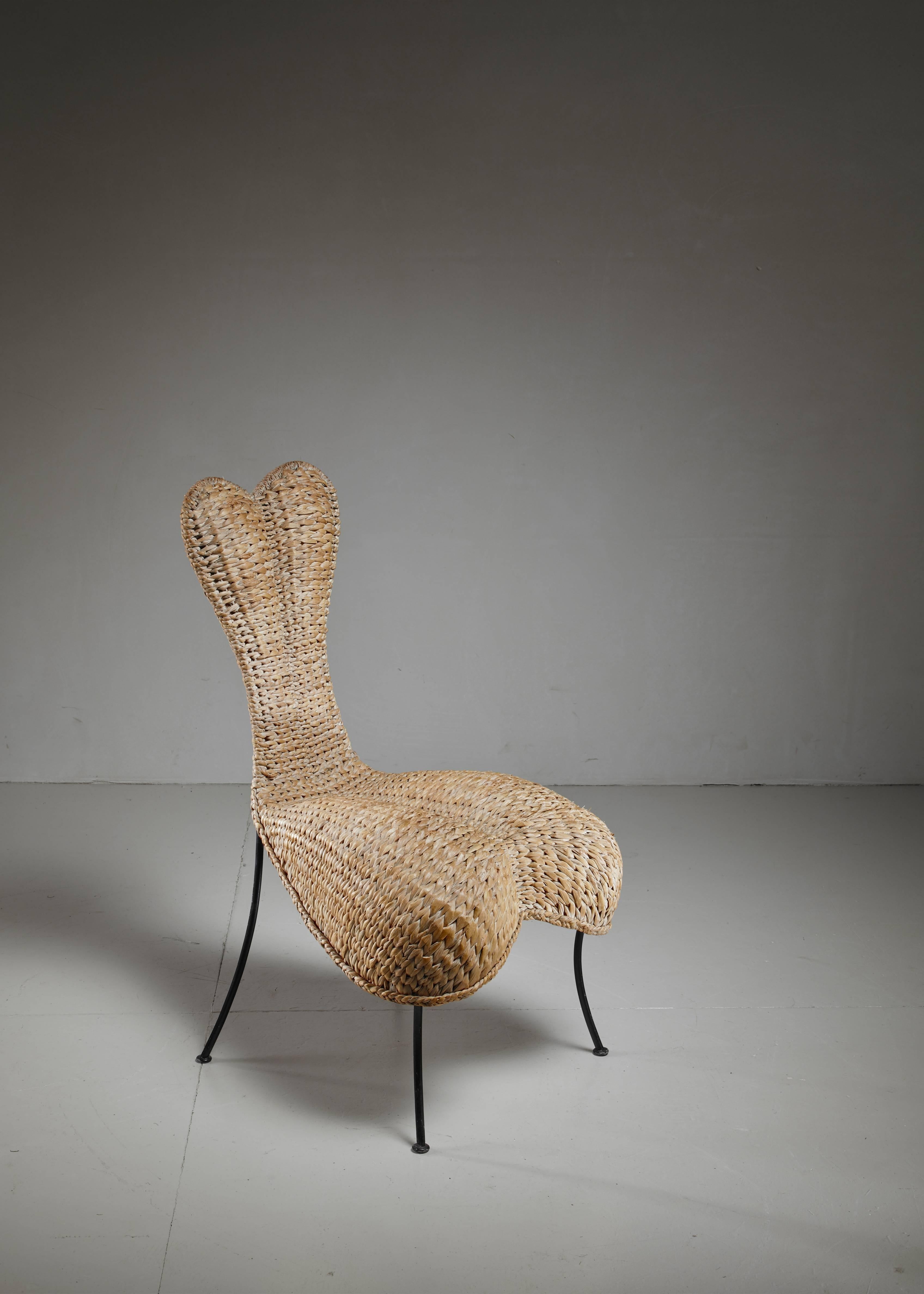 An anthropomorphic chair made of woven cane, standing on metal legs. Beautiful organic shaped object chair. 
 