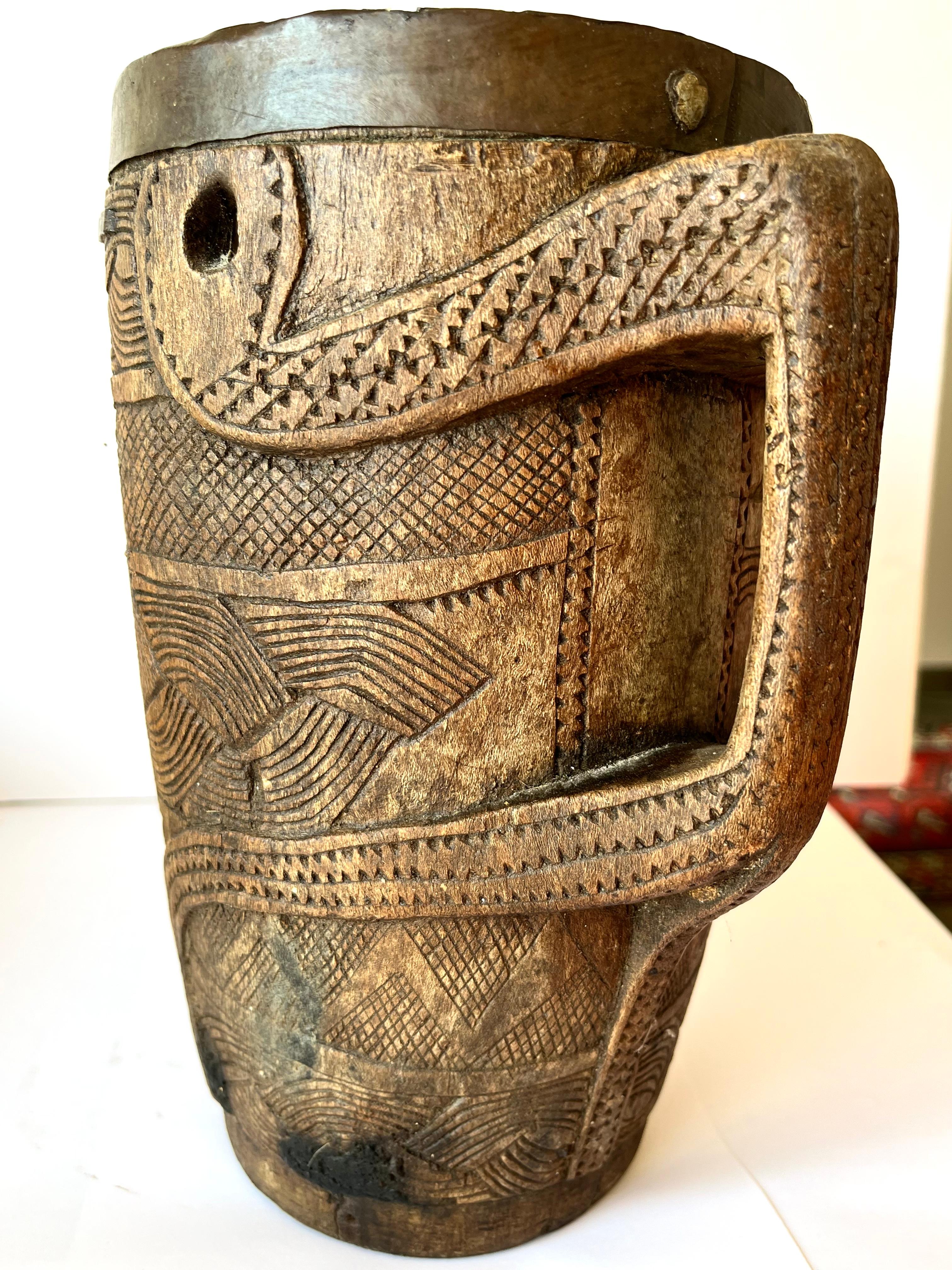 Large wood Nepal Yak Milk Jar hand crafted with geometric patterns covering the 
Body of the pot.
2 wholes around the top of the hedge where a rope went through in order to carry the jar .
Very great original patina .
An animal shaped figure is