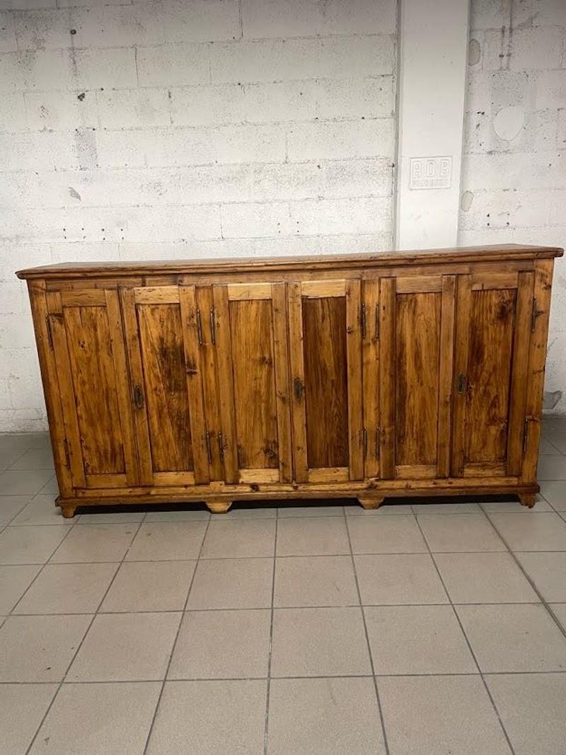 Antique rustic sideboard from the first half of the 1900s with 3 double doors with 3 shelves each inside.

The sideboard is of mixed softwoods and has old restorations that also characterize the historicity and lived-in nature of the furniture.

It