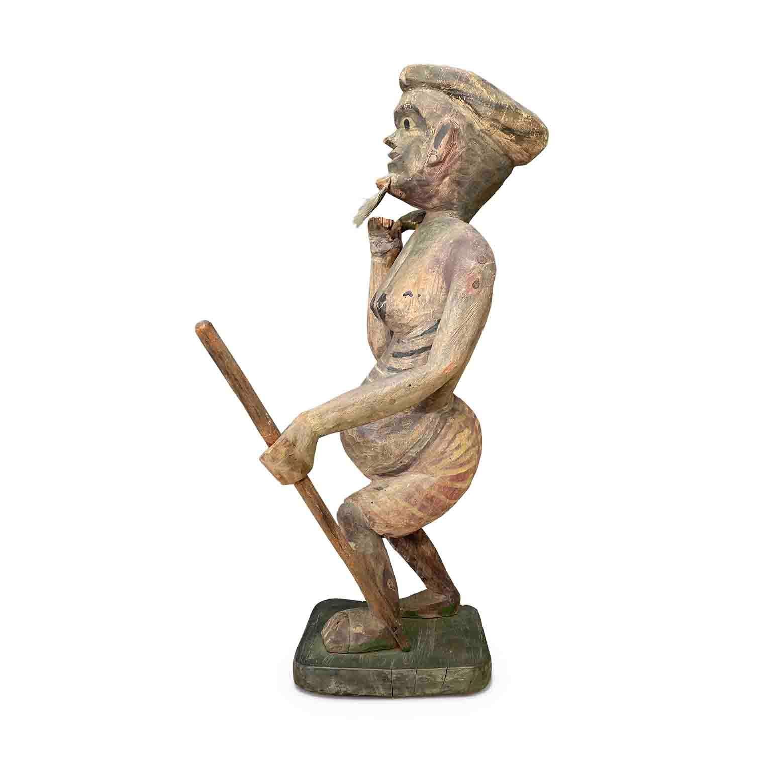 Antigua escultura de chamán, arte tradicional birmano de finales del siglo XIX, de pie sobre una base cuadrada se representa de pie con un bastón en la mano izquierda y una especie de calabaza y recipiente en la mano derecha. Lleva una falda roja