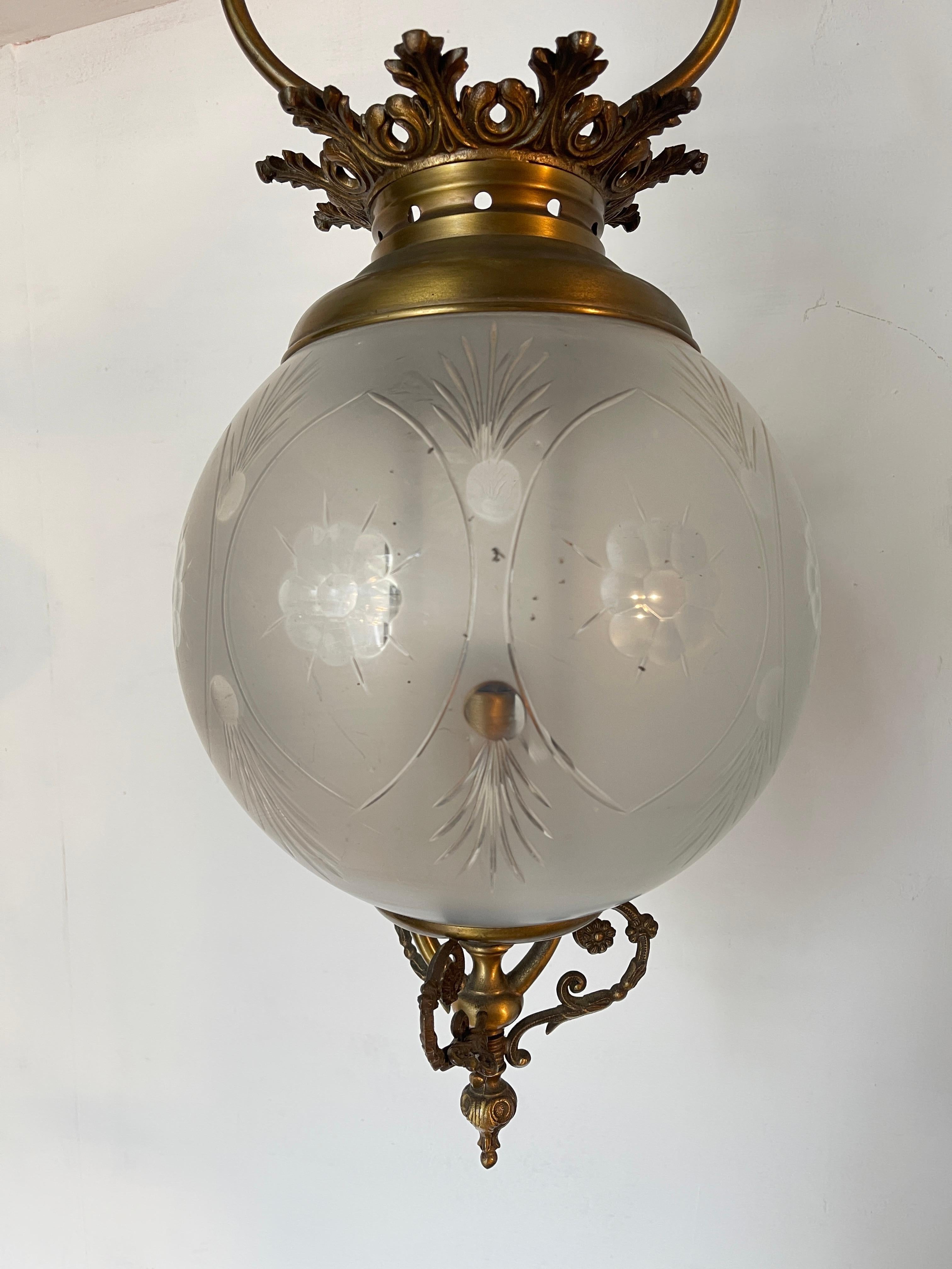 Lampadario stile vittoriano, probabilmente della fine del XIX o inizio XX secolo. Struttura in metallo (forse ottone o bronzo) con decorazioni floreali e dettagli elaborati. Paralume in vetro satinato o opalino, con incisioni decorative a motivi