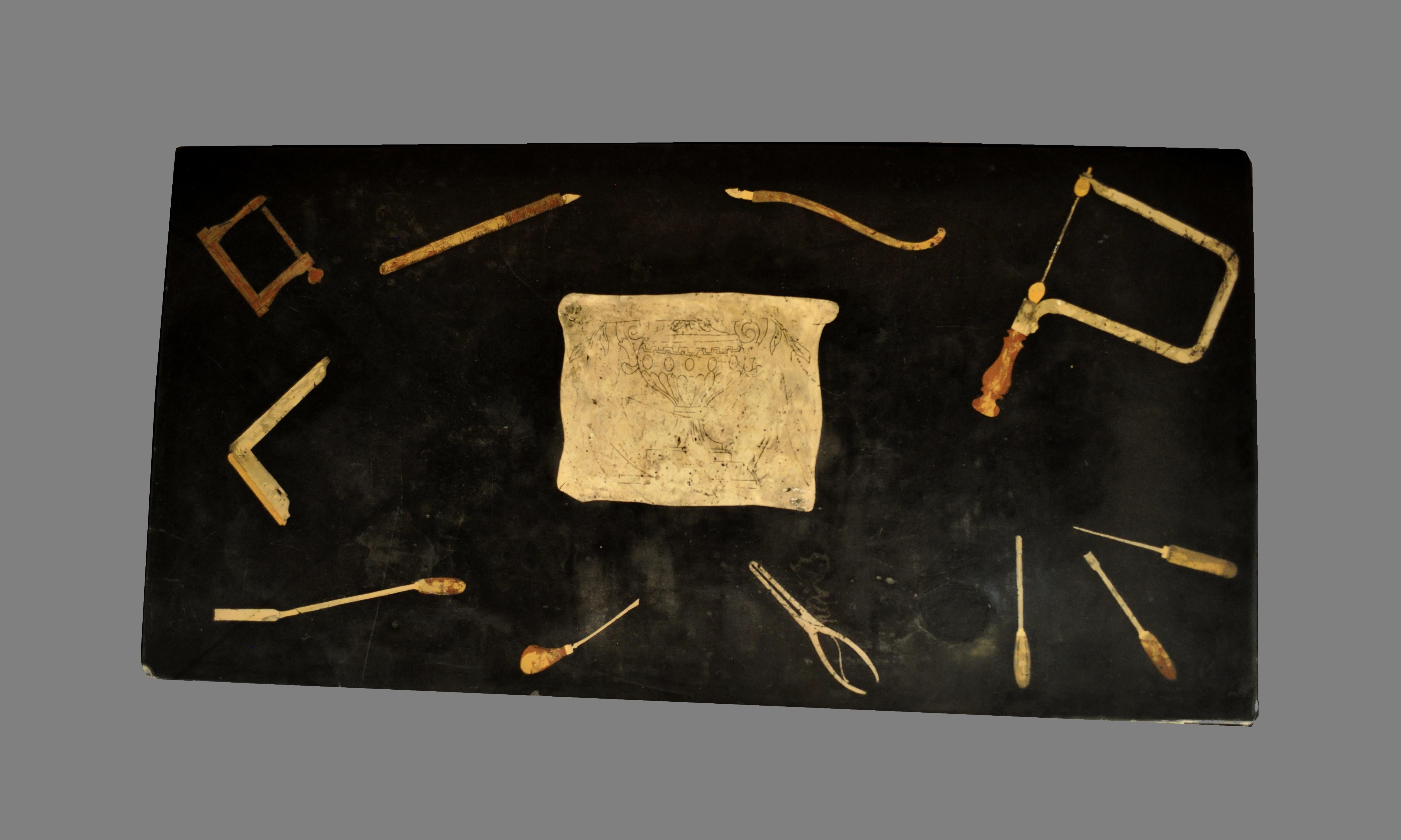 Antico piano in scagliola italiano con decoro raffigurante utensili da lavoro (forse gli attrezzi di uno scultore?) su fondo nero. Nel centro la riproduzione del disegno/bozza di un vaso.
Epoca XIX secolo.
Dimensioni: cm 121 (lunghezza); 61