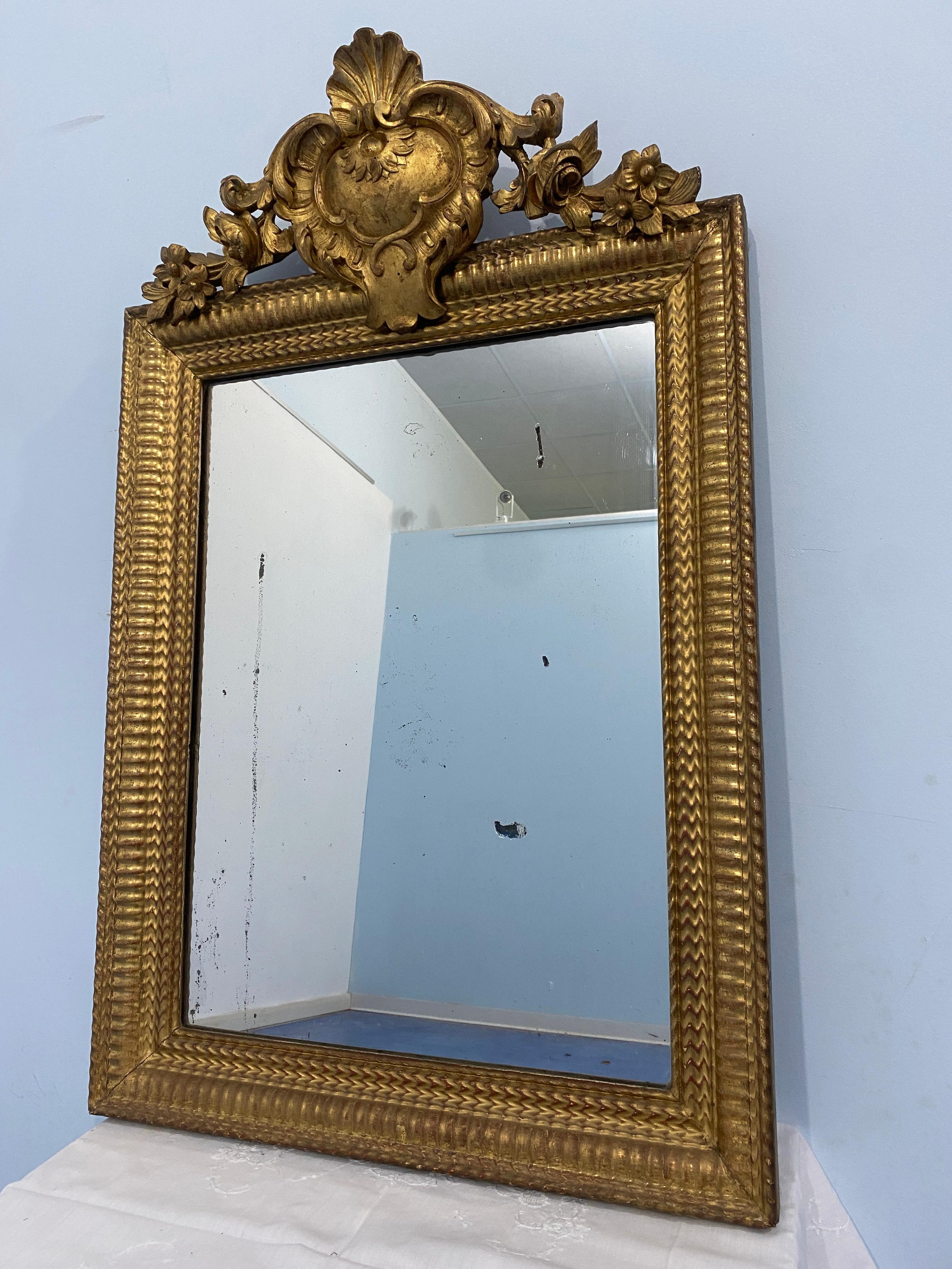 Antiker französischer Spiegel aus der Louis-Philippe-Ära, der mit Blattgold vergoldet ist. Das Design des Rahmens auf der Vorderseite ist sehr dekorativ und originell, ebenso wie das prächtige holzgeschnitzte Gesims mit floralen Motiven an den