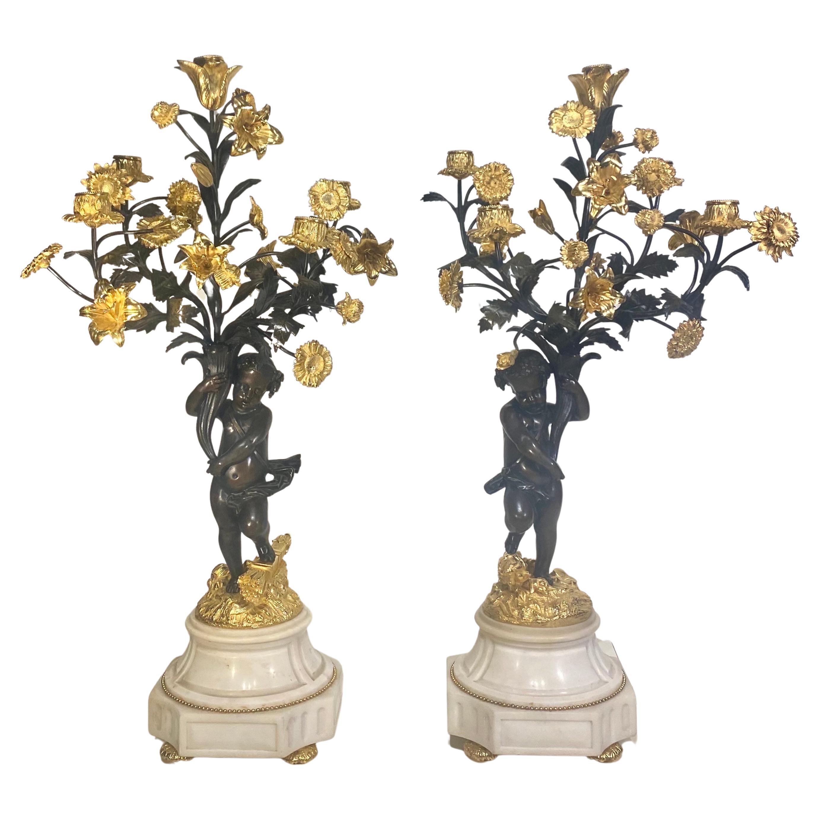 A fine true pair of patinated bronze, ormolu and white marble figural Cherub candelabra in excellent condition. Set upon a white marble base, with ormolu beads surrounding the marble. 
The putti stand upon rocks, holding up the five branch stems,