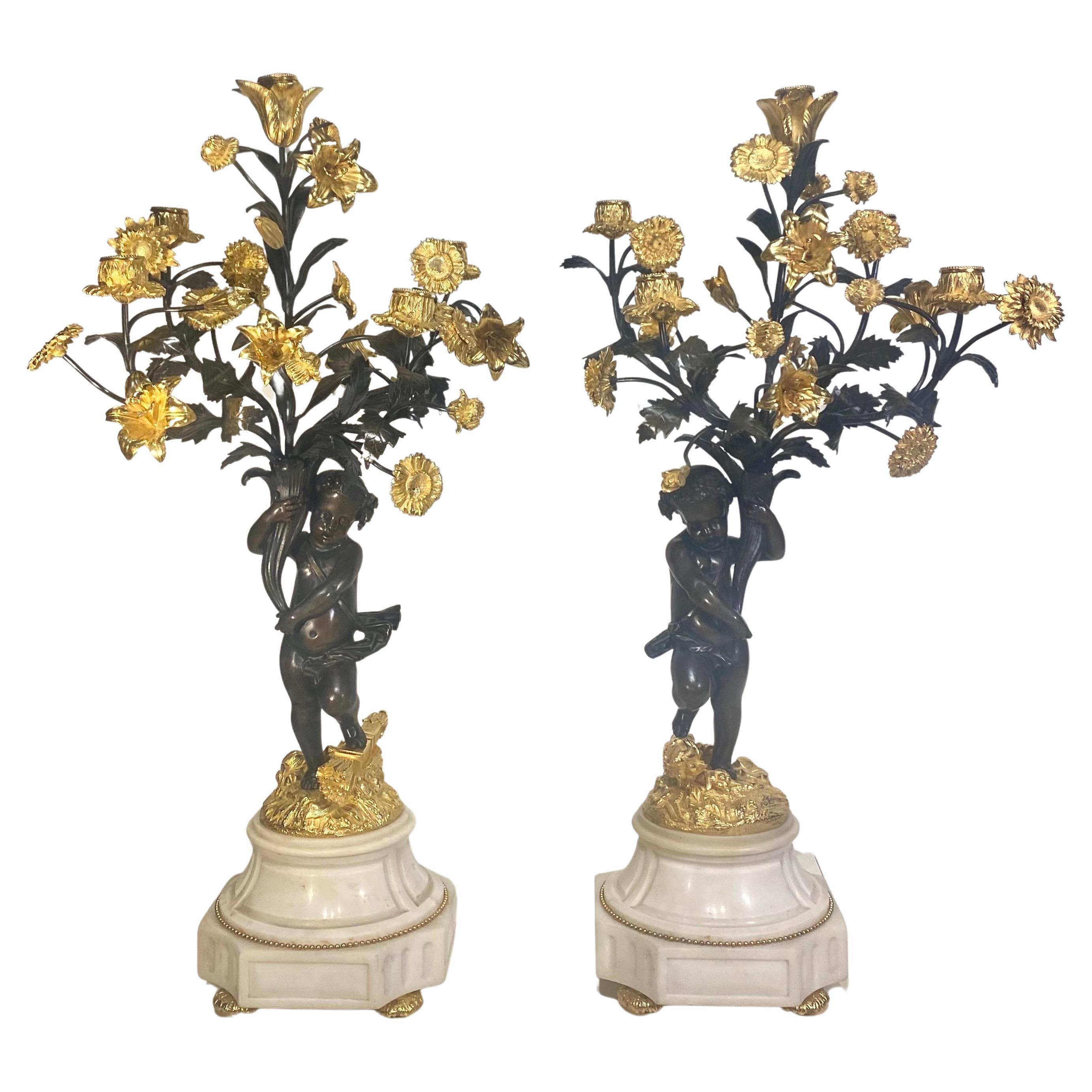 Una bella coppia di candelabri con figure di cherubini in bronzo patinato, ormolu e marmo bianco in ottime condizioni. La base è in marmo bianco, con perline in ormolu che circondano il marmo. 
I putti stanno in piedi sulle rocce e sorreggono i