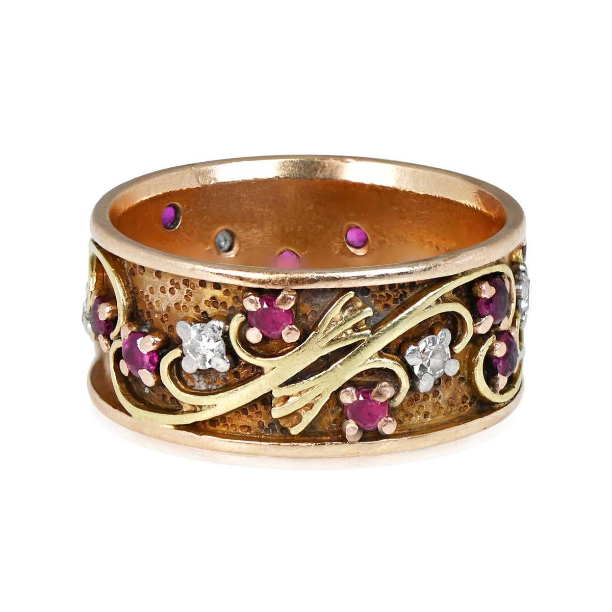 An exquisite antique wedding band from the Art Nouveau era, circa 1890. This timeless piece showcases a floral scroll-motif design adorned with round-cut natural rubies and single-cut diamonds. The stones beautifully contrast against a mottled