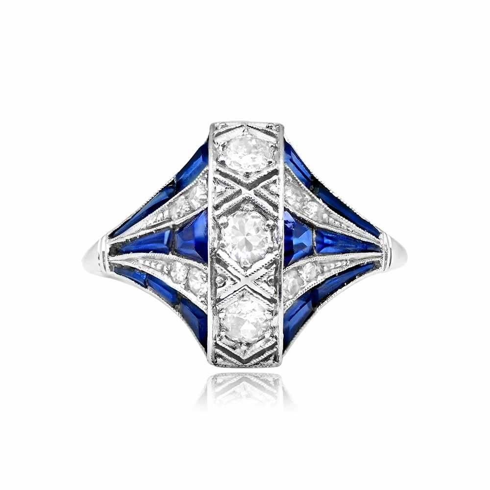 An exquisite antique engagement ring boasting a vertical row of three old European cut diamonds. The center diamonds are accented on each side by graduating layers of diamonds and synthetic sapphires, creating a captivating design. The total