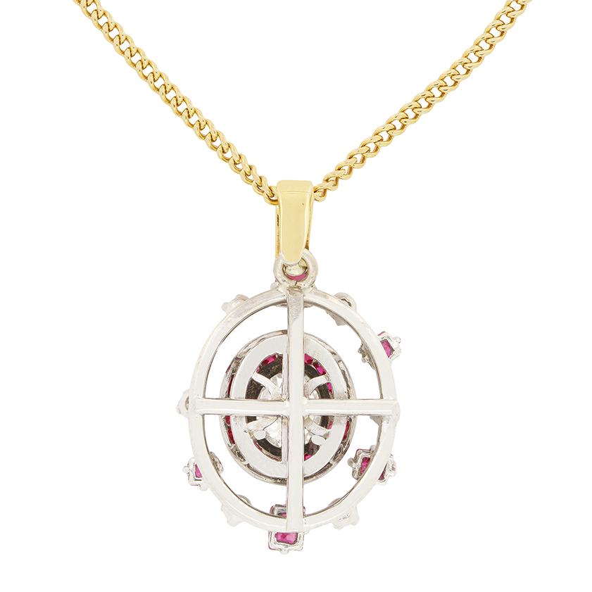 Ce pendentif cible antique est un chef-d'œuvre d'élégance des années 1930. En son centre se trouve un diamant de taille ovale ancienne, serti clos, pesant 0,85 carats, de couleur J et de pureté SI1. Autour de la pierre centrale, un halo de baguettes