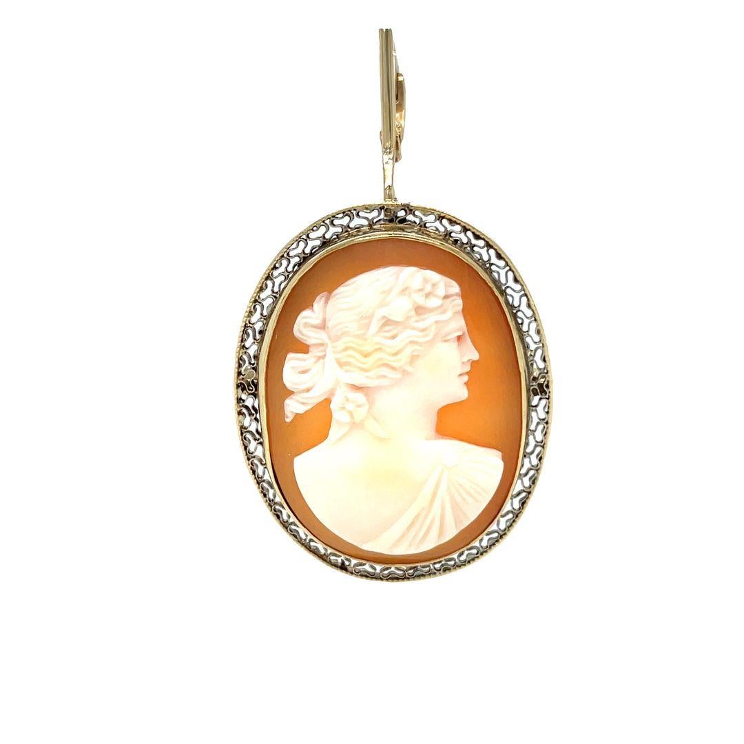 This lovely cameo captures the serene profile of a woman gracefully adorned with swept up flowing locks highlighted by two decorative flowers. This hand carved conch shell cameo is decoratively framed by a 10 karat yellow gold lacey filigree bezel
