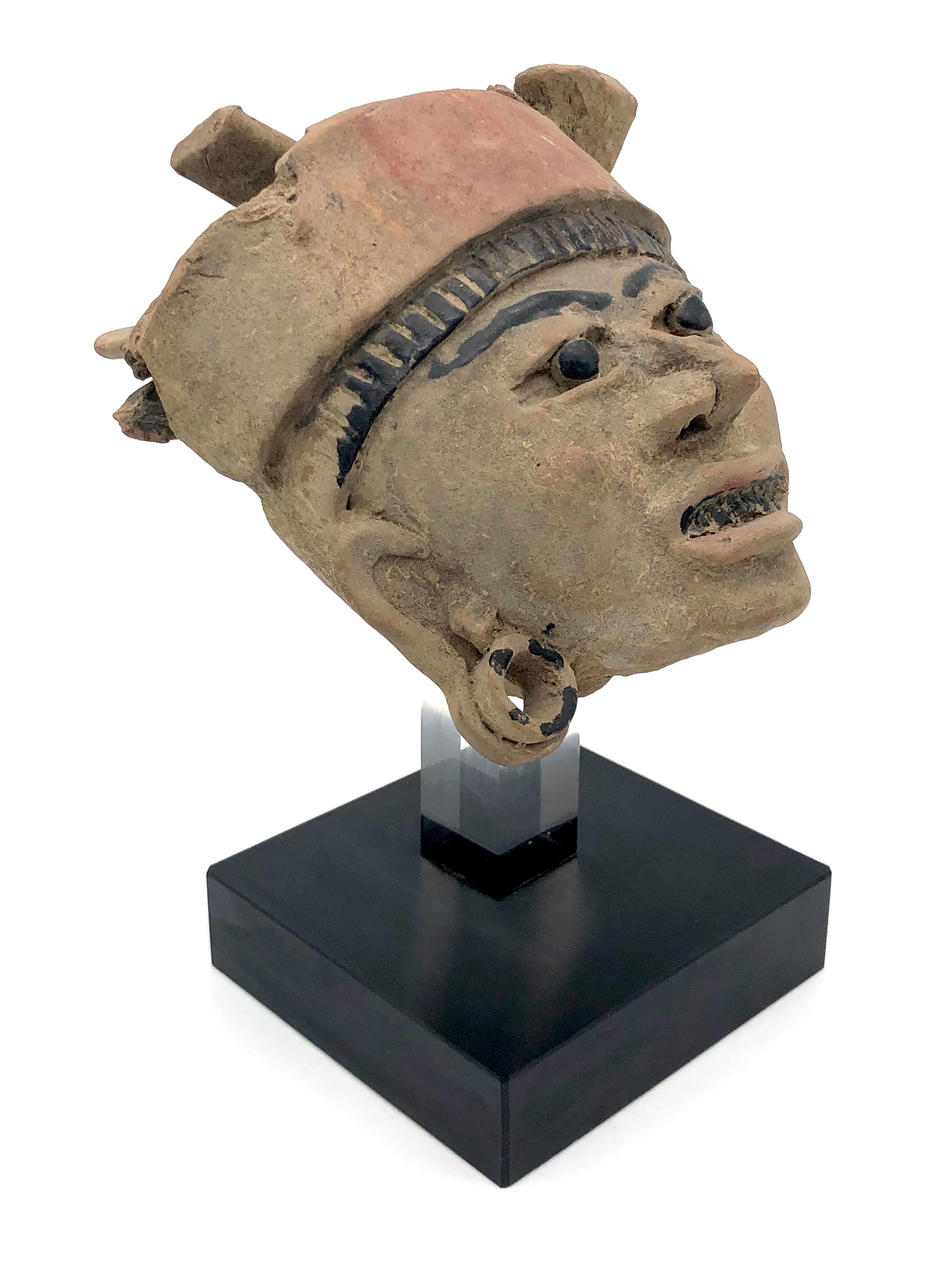 Diese ausdrucksstarke Skulptur des Kopfes eines Kriegers ist aus Terrakotta gefertigt und mit schwarzer Farbe bemalt.
Sie stammt aus der Remojadas-Kultur in der mexikanischen Küstenregion Veracruz.

Die Höhe des Kopfes ohne Ständer beträgt 16 cm.