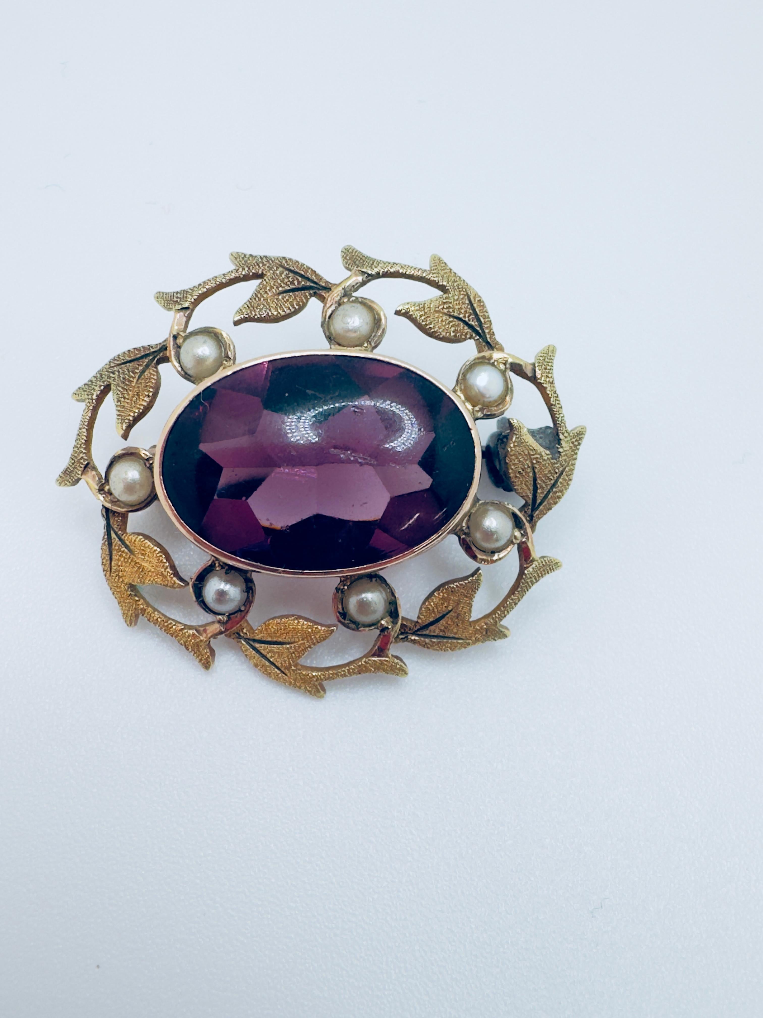Este exquisito broche antiguo está finamente elaborado en oro de 10 quilates y destaca una impresionante amatista talla cabujón como punto focal. Con unas medidas aproximadas de 16x12 mm, la amatista revela un profundo y regio color morado con una