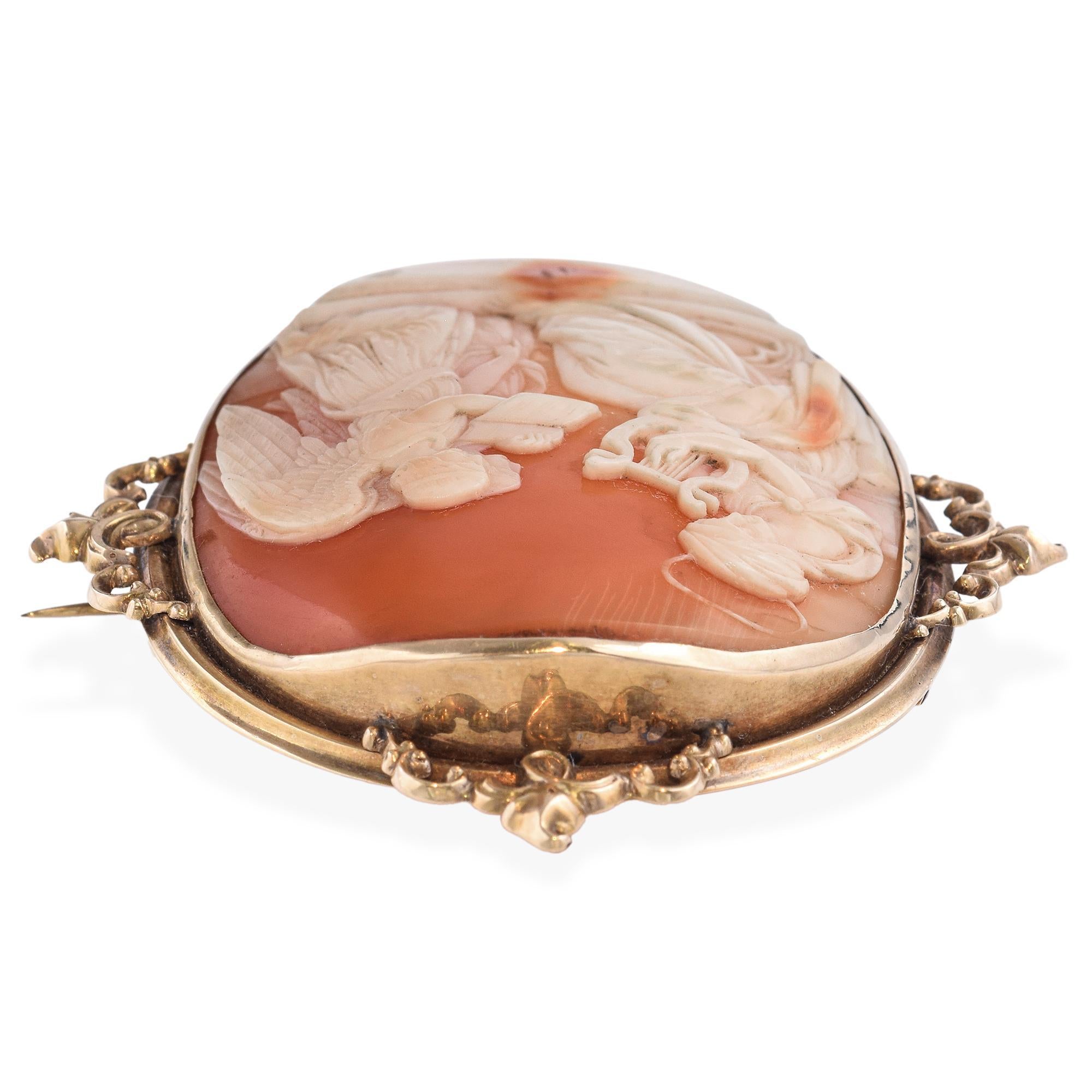 An antique cameo brooch depicting a saint gracefully playing a lyre before two angels, evoking a scene of celestial music and divine serenity. The intricately carved cameo is set in a 10K yellow gold frame adorned with ornate scrollwork at the top,