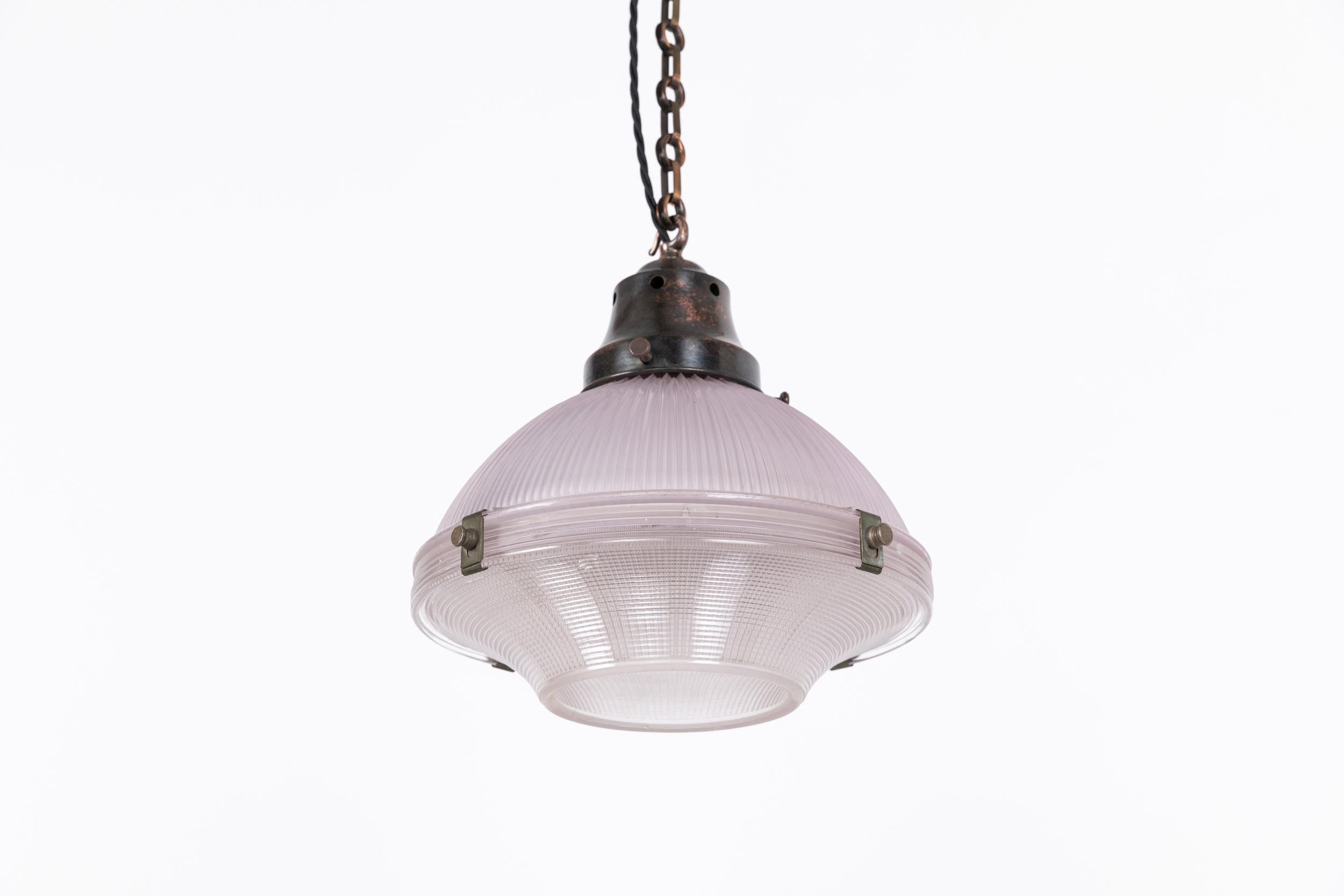 Una lampada a sospensione 'Reflector-Refractor' da 12 pollici prodotta in Inghilterra da Holophane. c.1920.

Riflettore in vetro prismatico in due parti con tonalità violacea sostenuto da una galleria in rame patinato. Tutte le parti in vetro hanno