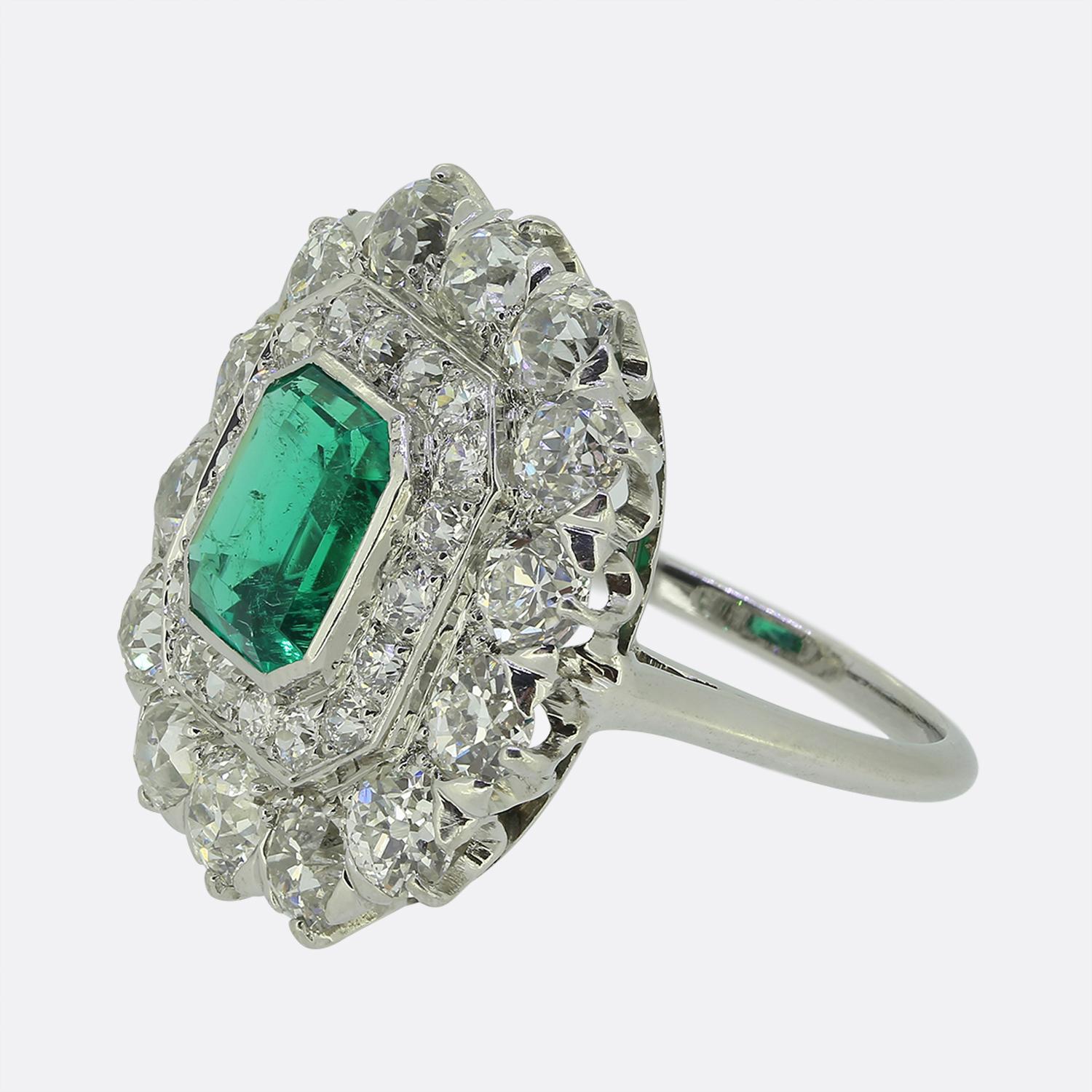 Cette magnifique bague à grappes met en valeur une émeraude d'un vert éclatant en son centre, taillée de manière experte pour attirer le regard. Cette pierre principale est légèrement surélevée dans une élégante monture rub-over, tout en étant