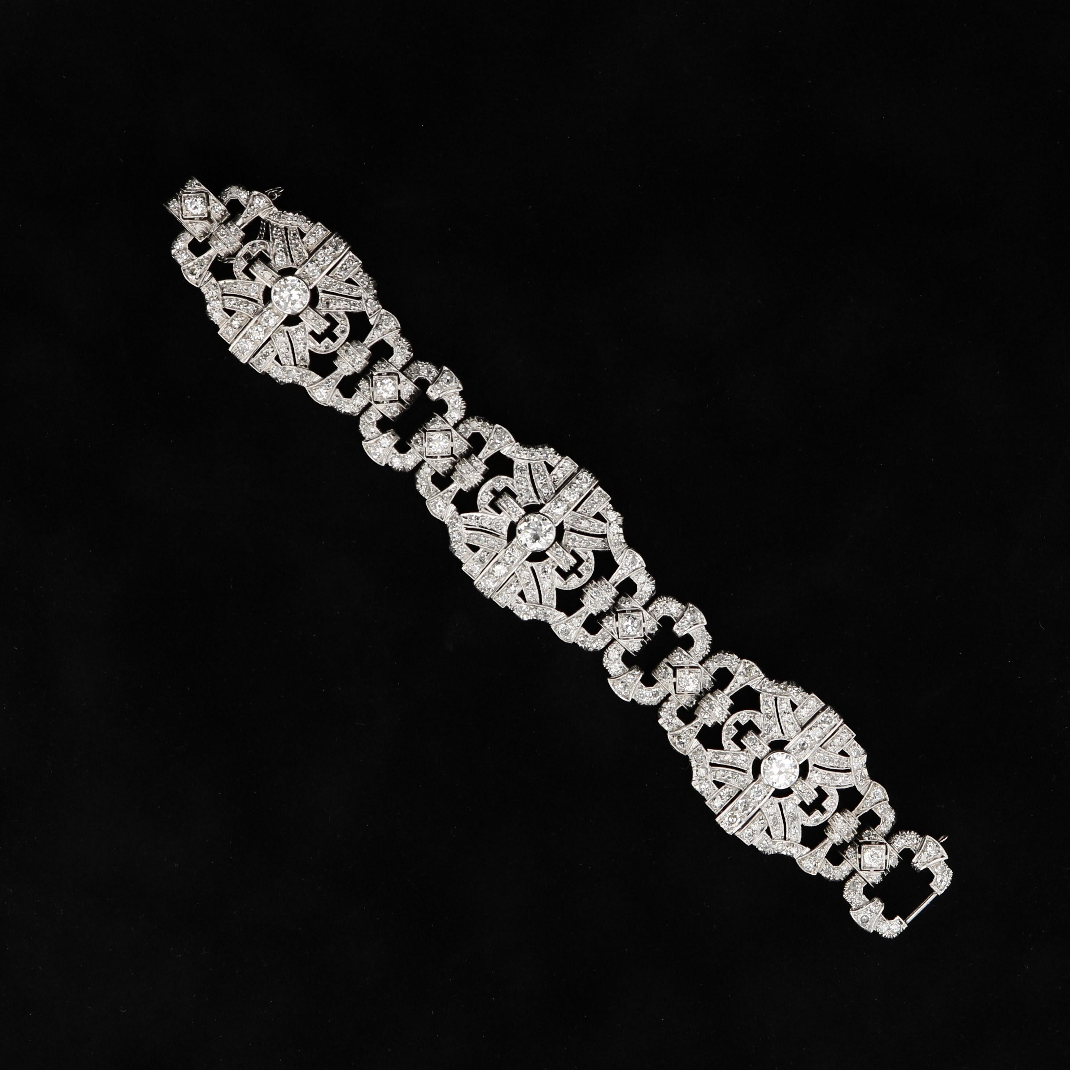 This antique platinum and diamond bracelet features approximately 12.00 carats of bright white round diamonds. The elaborate design of open arches and bows is cast in platinum with fine millegrain detailing.  The integrated clasp all but disappears