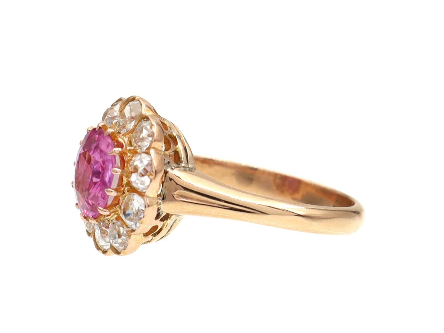 Antique 1.20ct fancy pink sapphire and diamond cluster ring in 18kt yellow gold. Centrally set with an estimated 1.20 cushion shape mixed cut fancy pink sapphire in a raised claw setting, encircled by a row of round Old Mine cut diamonds in grain