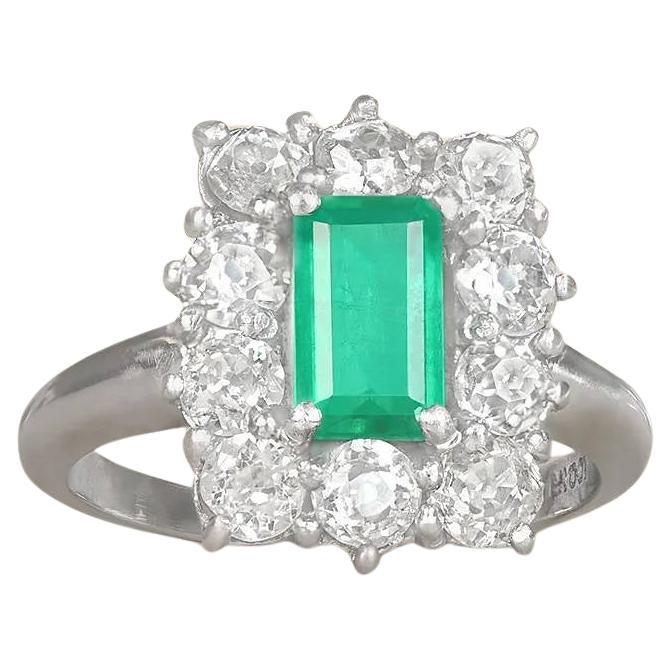 A stunning antique ring showcasing a natural Colombian emerald-cut emerald weighing approximately 1.25 carats, elegantly set in prongs. Surrounding the center stone is a halo of old European cut and mine cut diamonds, prong-set with a total