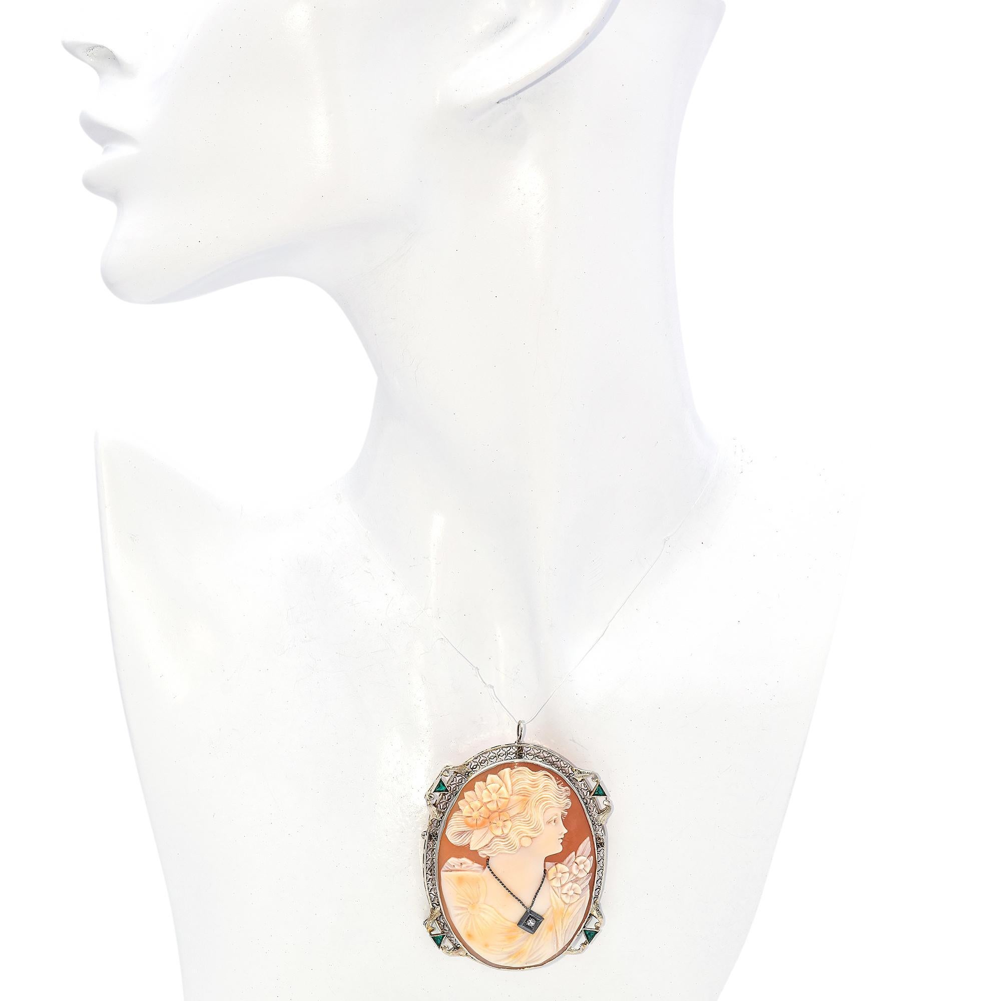 This exquisite brooch showcases a finely carved cameo of a woman's profile, adorned with delicate flowers. The cameo is encased in a 12K gold filigree frame, beautifully embellished with vibrant green trillion-cut emeralds. A sparkling old mine-cut