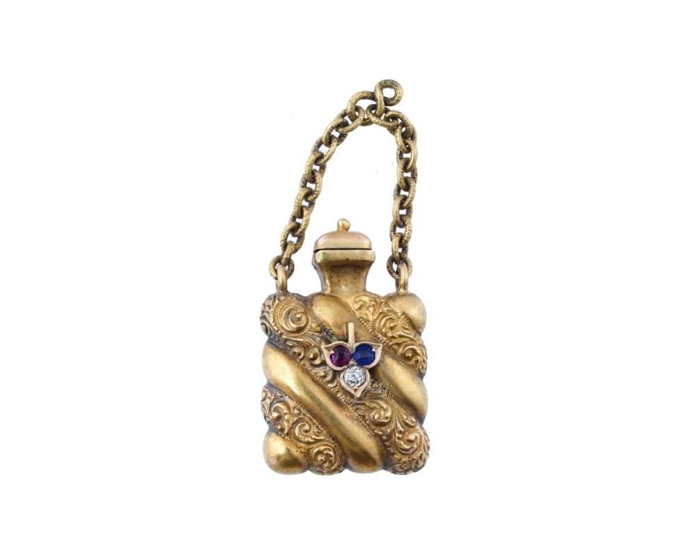 An antique Victorian 14K gold perfume bottle, circa the mid 19th century. The piece is modeled as a miniature vessel of a gadrooned square shape, adorned with fine hand carved patterns and set with a ruby, a sapphire and a diamond to the front side.