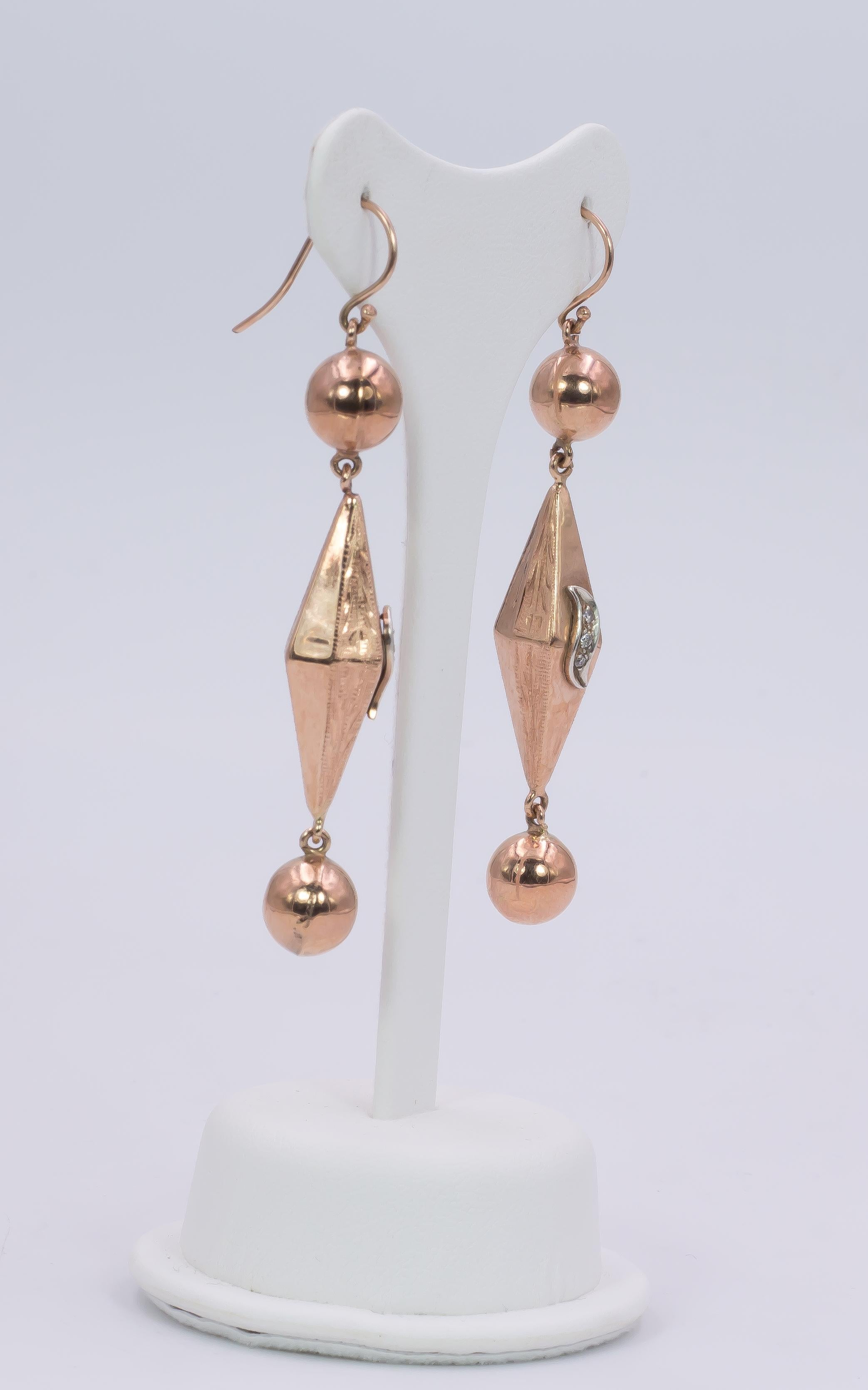 An exquisite pair of antique pendant earrings, crafted in 14K rose gold; each one is set with an upper and a lower sphere, linked to a central pyramidal section, decorated with diamonds. 
The earrings are antique and date from the