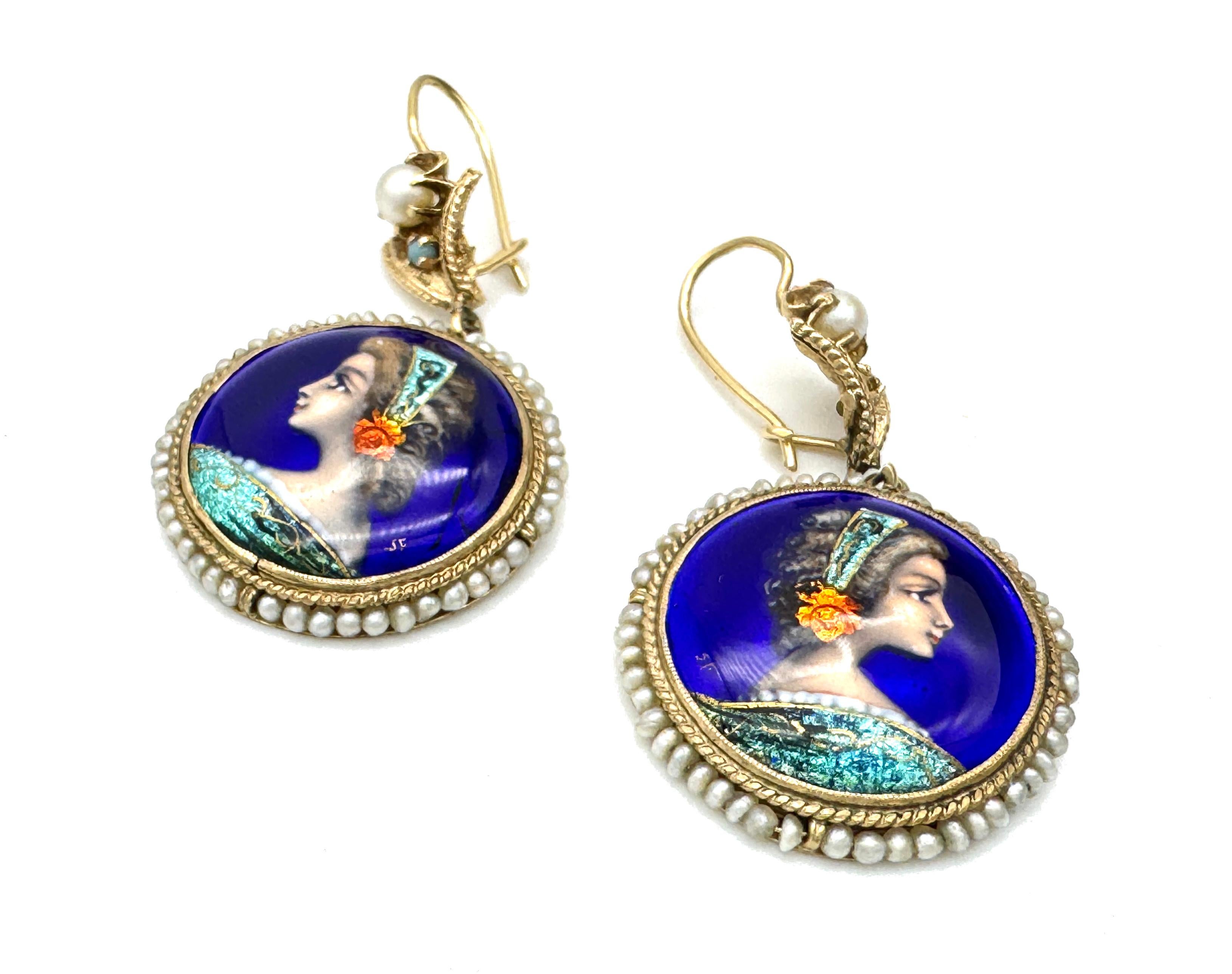 Cette paire de boucles d'oreilles pendantes en émail a été créée en 1880 ca.
Elles sont constituées de peintures rondes en émail représentant une jeune femme de profil portant un bandeau de brocart vert turquoise orné d'une rose. La robe de la jeune
