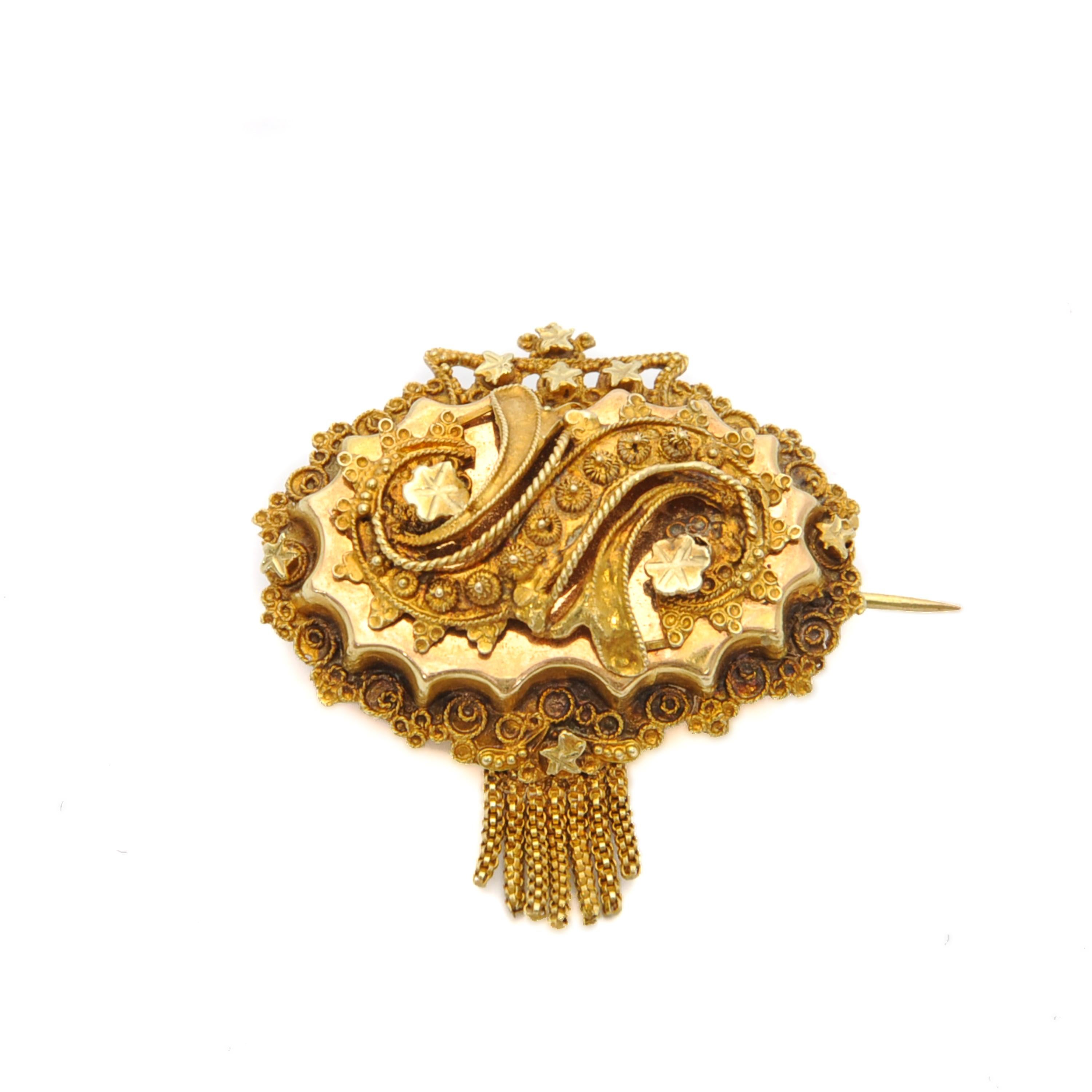 Il s'agit d'une broche ancienne en or 14 carats du 19e siècle, créée avec un fin travail de cannetille. La broche de forme ovale est ornée de cannetilles, d'étoiles et d'une couronne sur le dessus. La broche est sertie de sept glands qui se