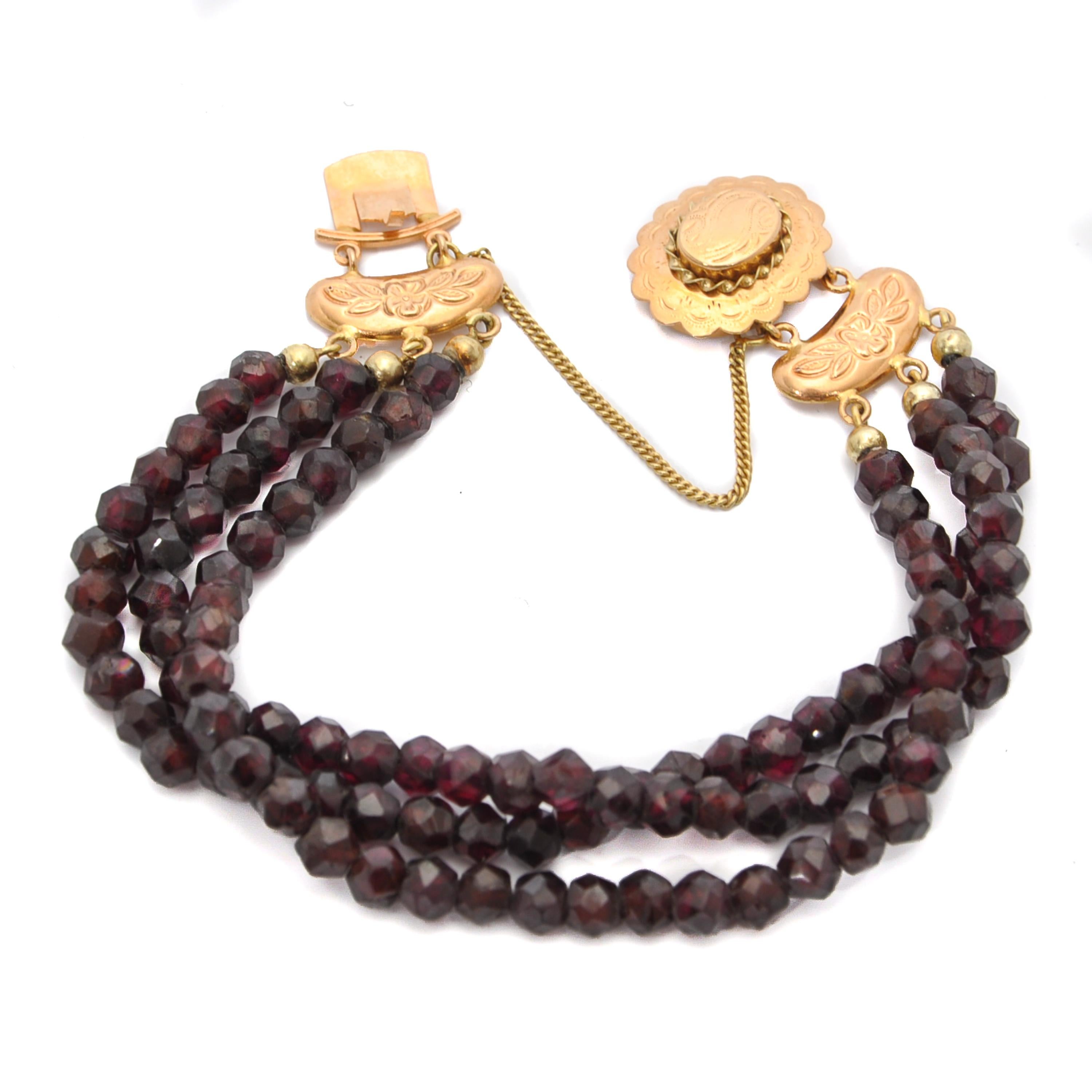 This is an antique jewelry set consisting of a three-strand 14 karat yellow gold garnet bracelet and a 14 karat gold garnet two strand necklace. The oval-shaped clasp of this set is beautifully engraved with a floral design, detailed figures and a